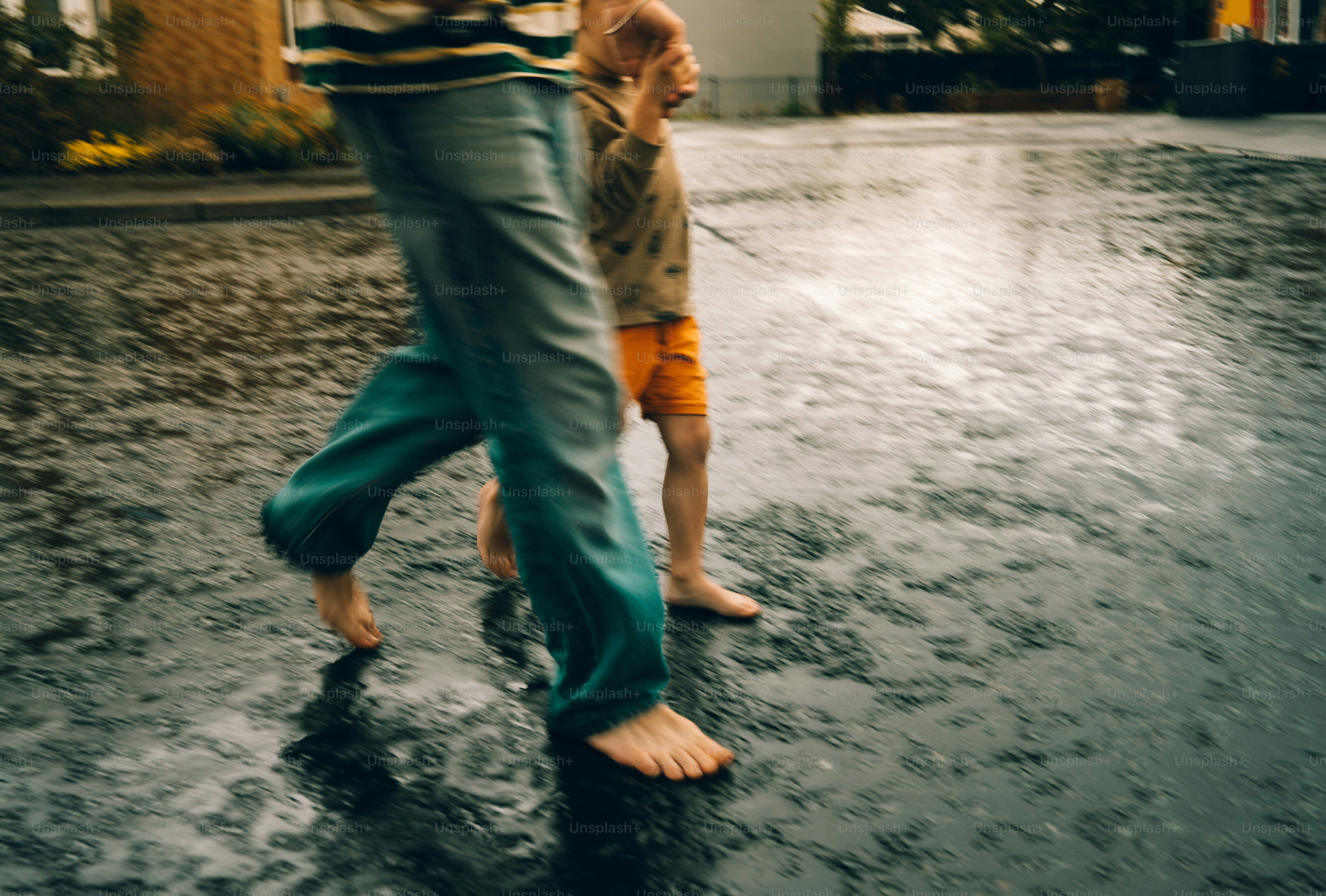 Two barefoot people walk on wet pavement