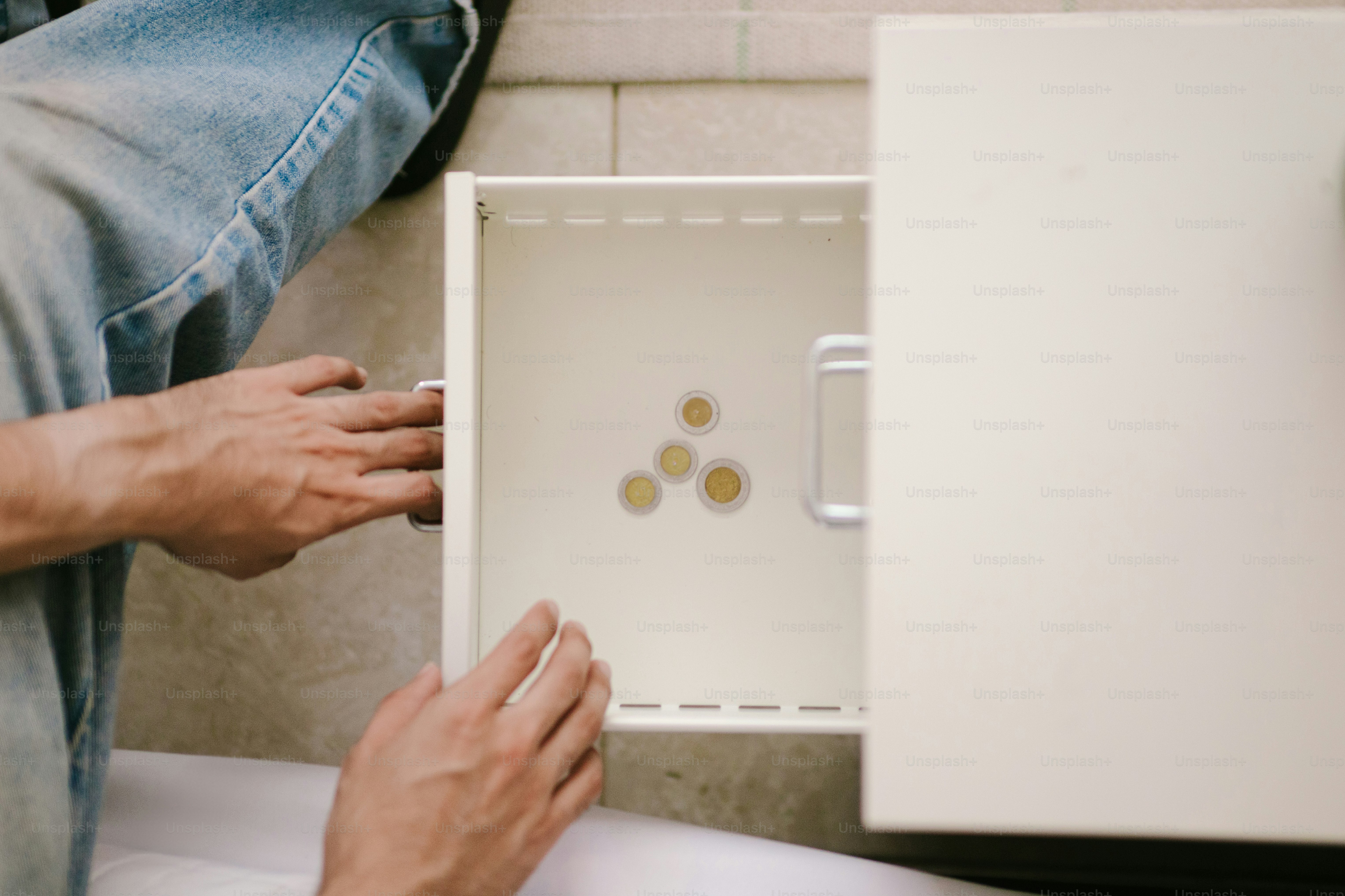 Des mains plongent dans un tiroir ouvert avec des pièces de monnaie.