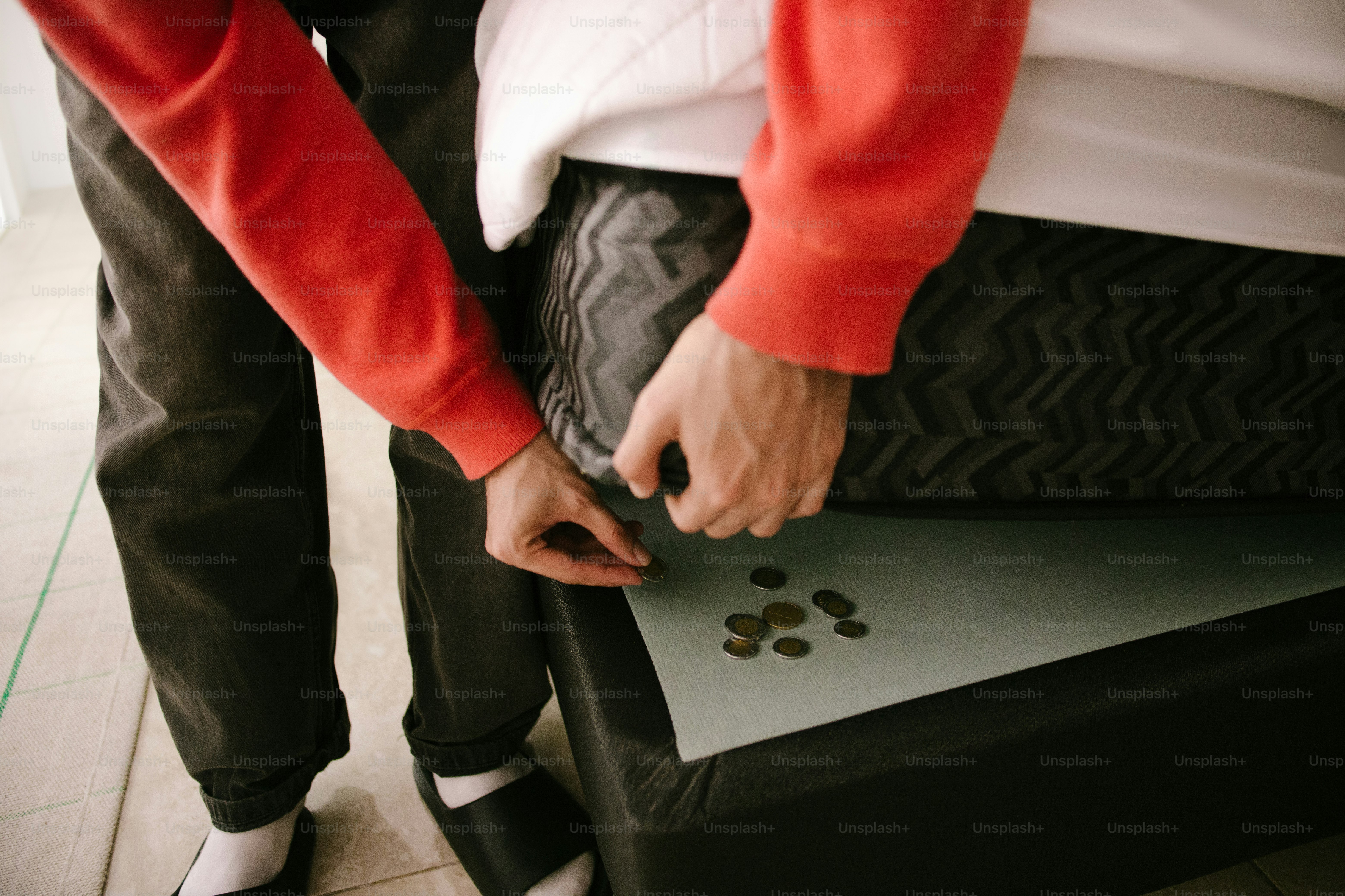 Person placing coins under mattress corner.