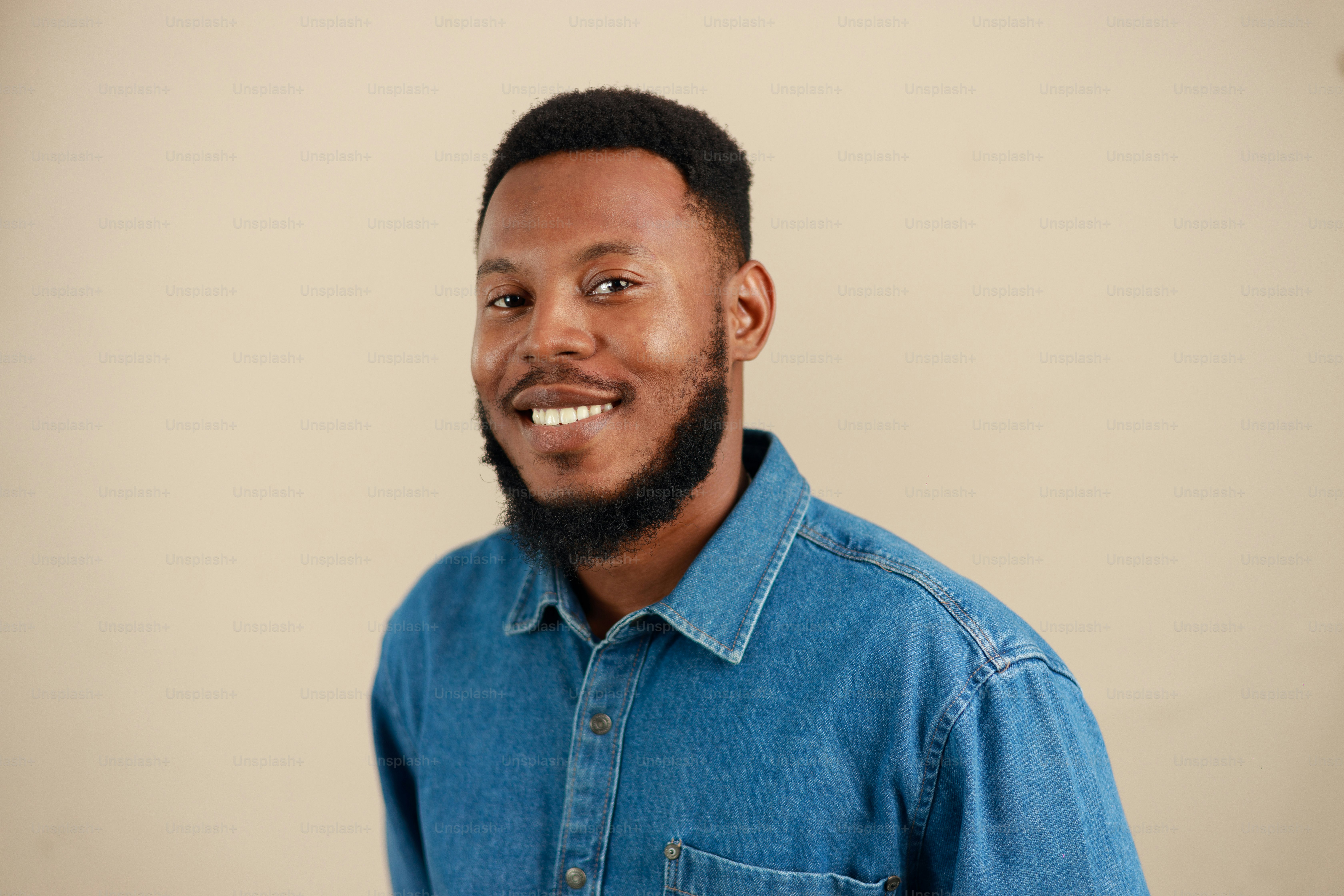 A smiling man with a beard in a denim shirt.
