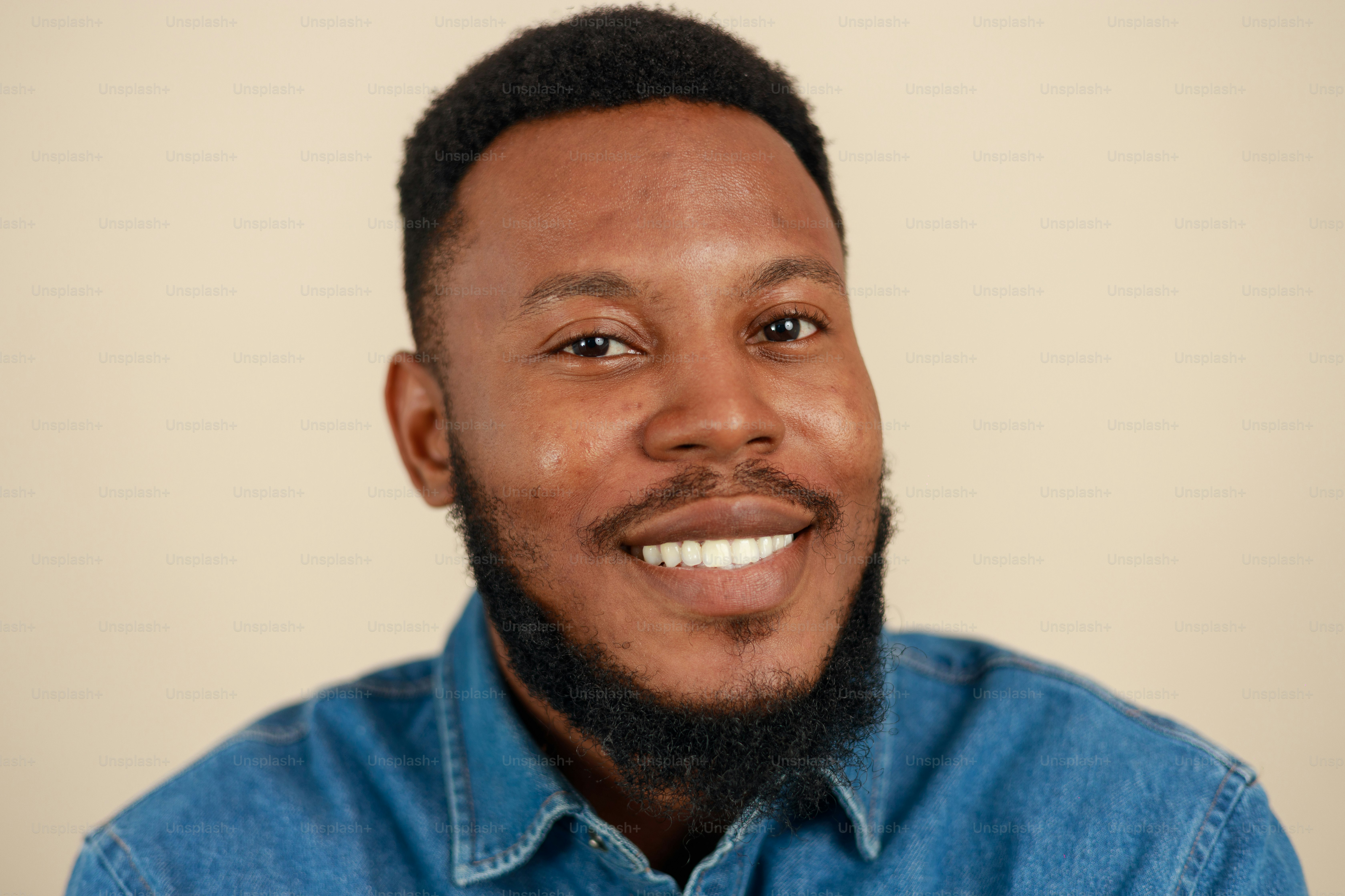 A smiling man with a beard in a denim shirt.