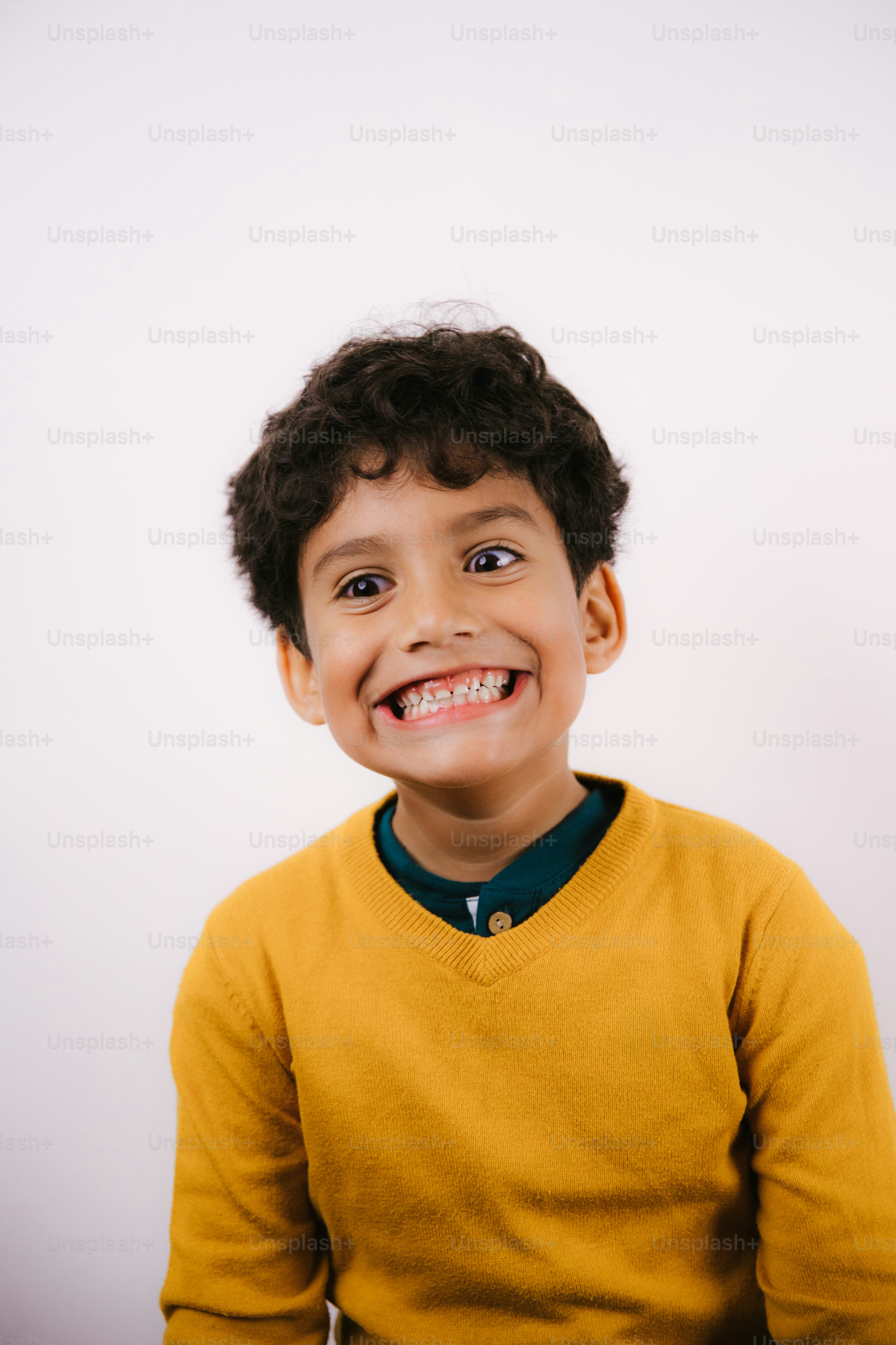 A young boy with curly hair smiles widely.