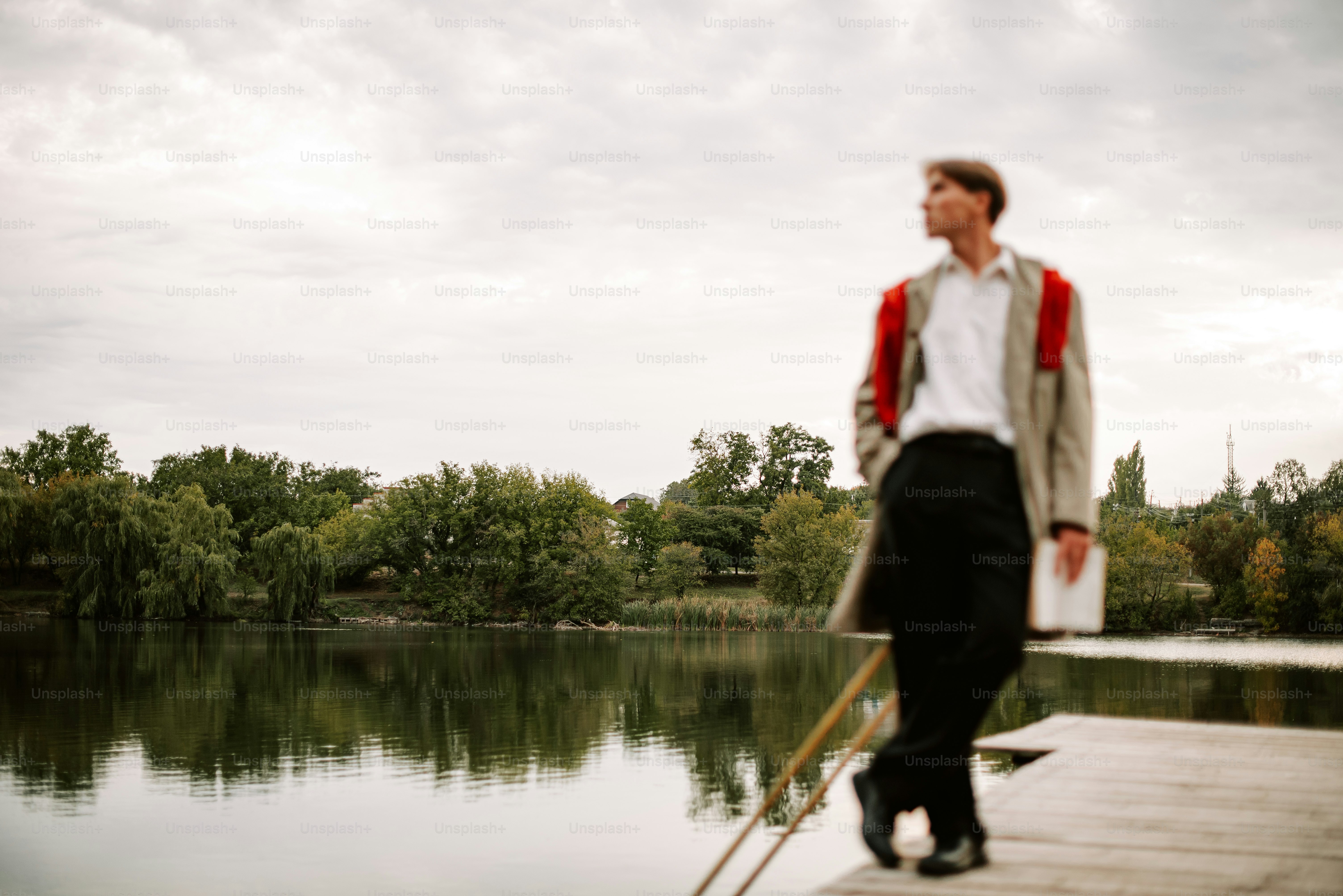 Man in stylish coat on a dock by the lake.
