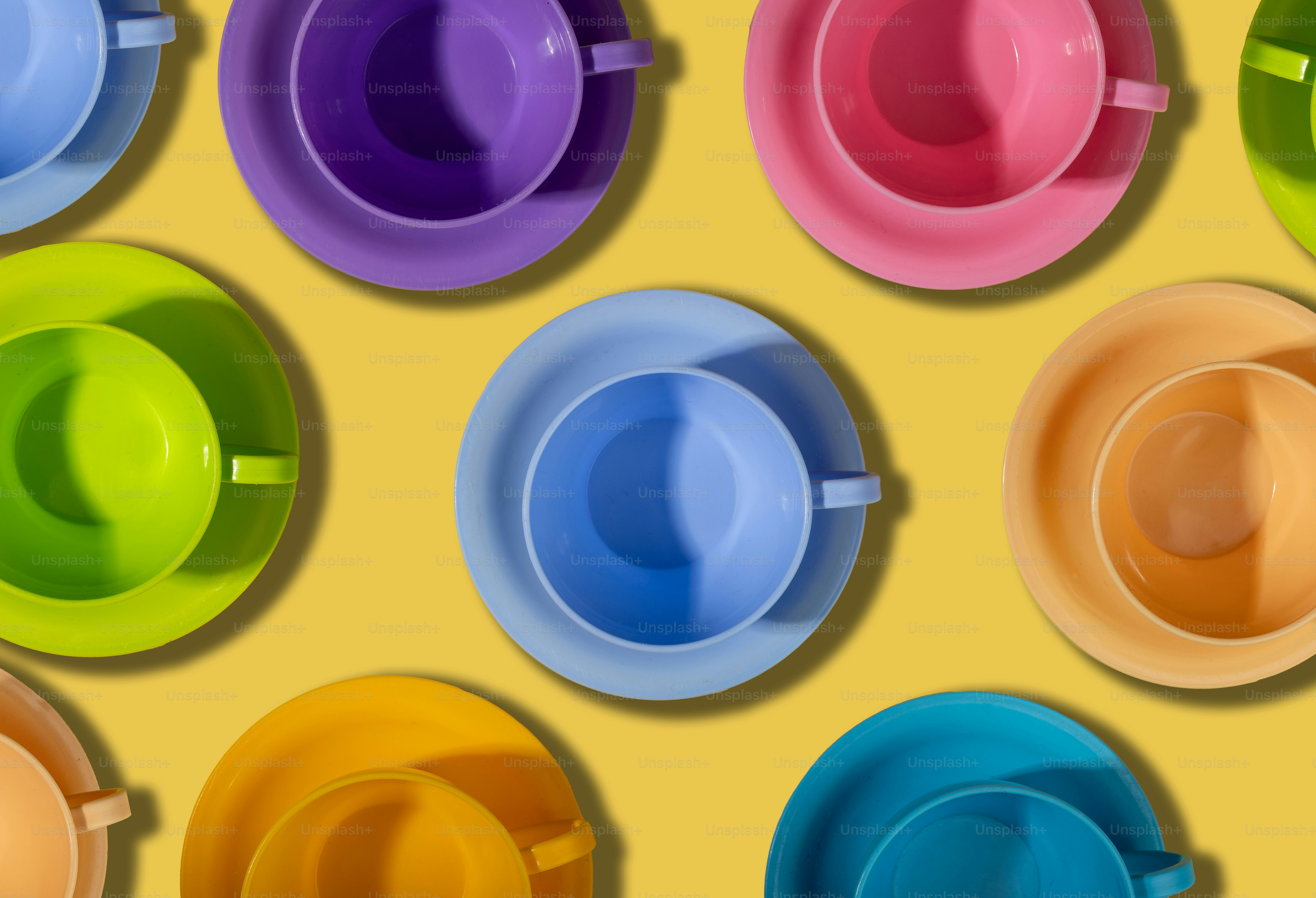 Tazze da tè e piattini colorati disposti su sfondo giallo