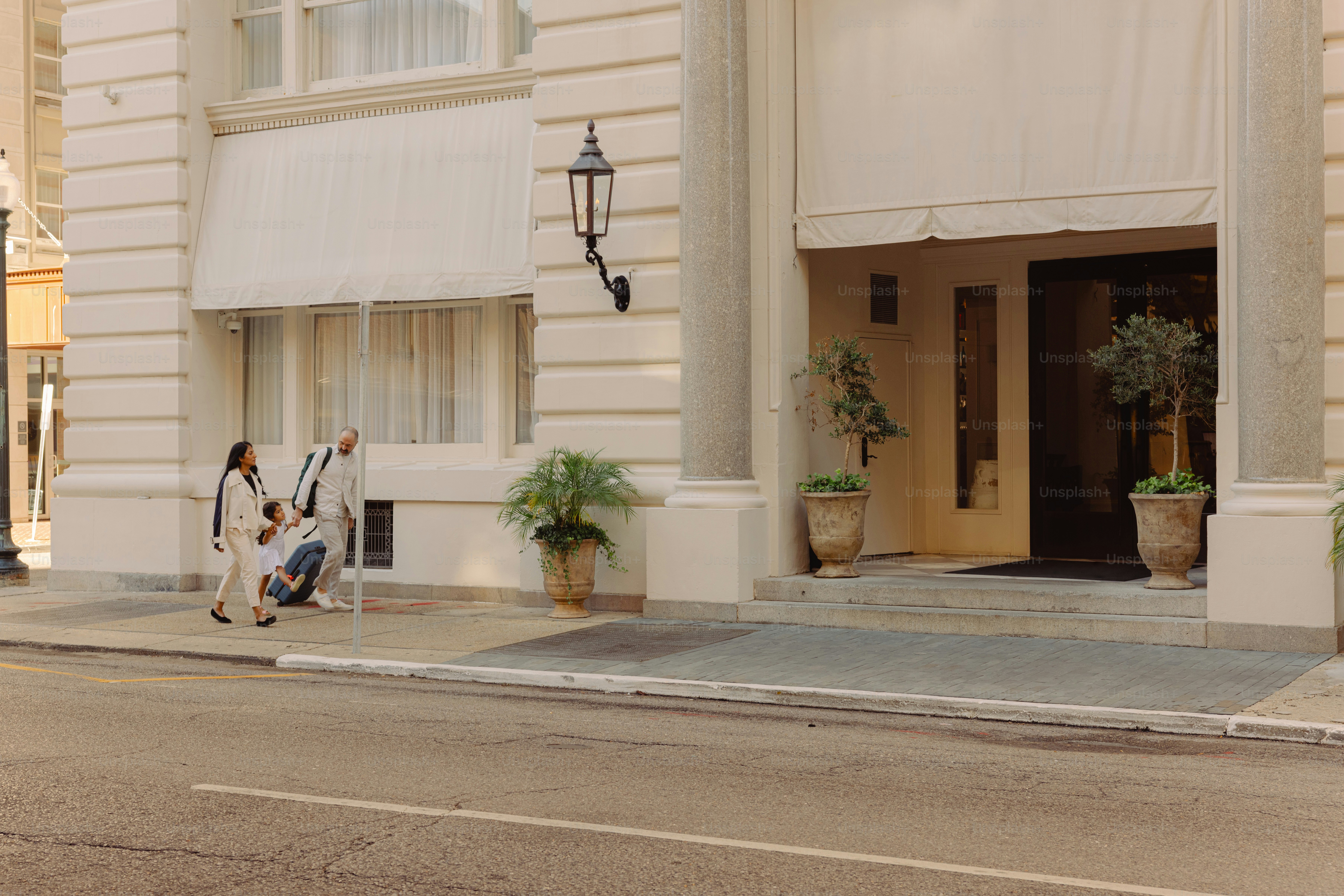 Two people walk past a building entrance with plants. photo – Travel ...