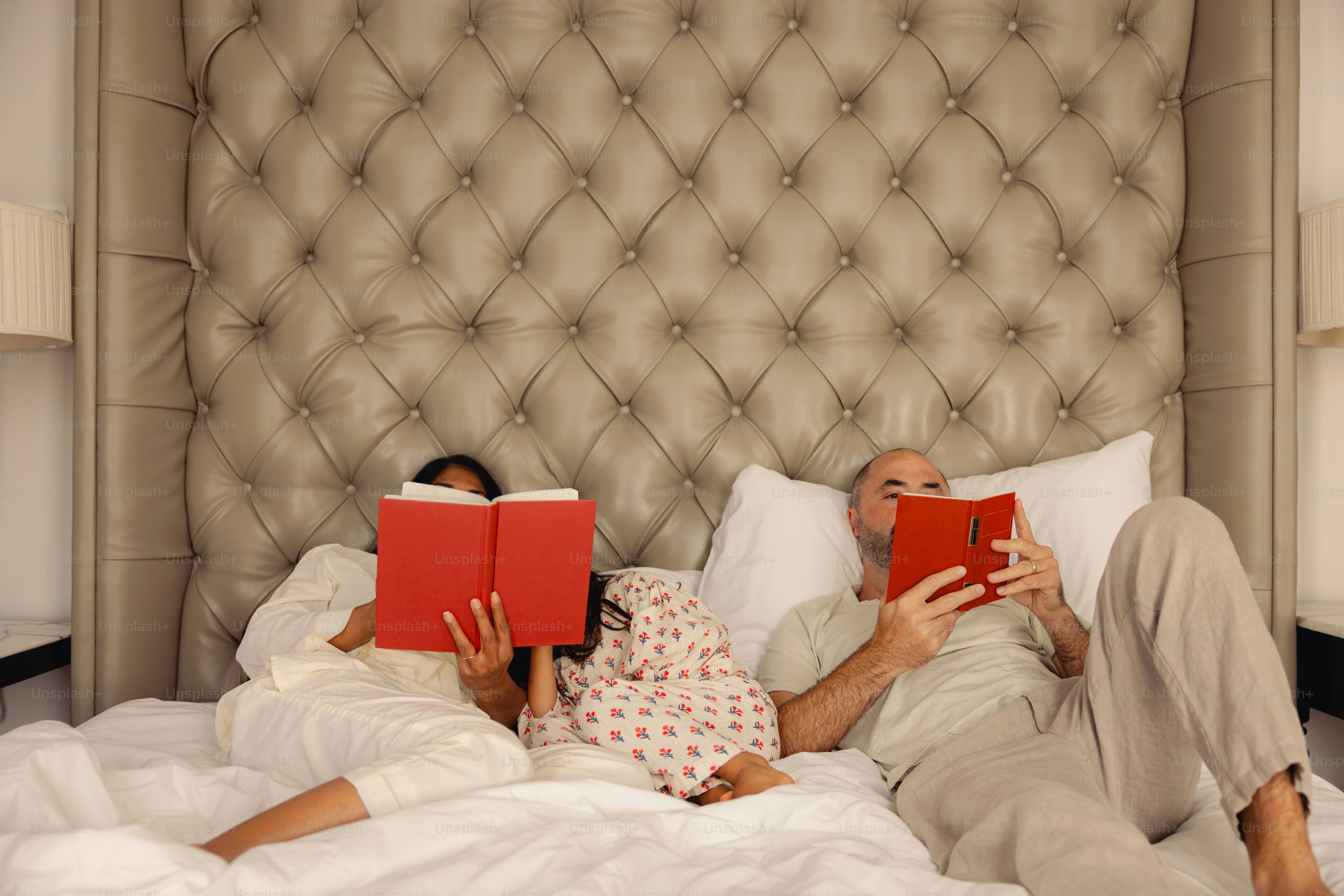 Paar liest Bücher in einem getufteten Bett.