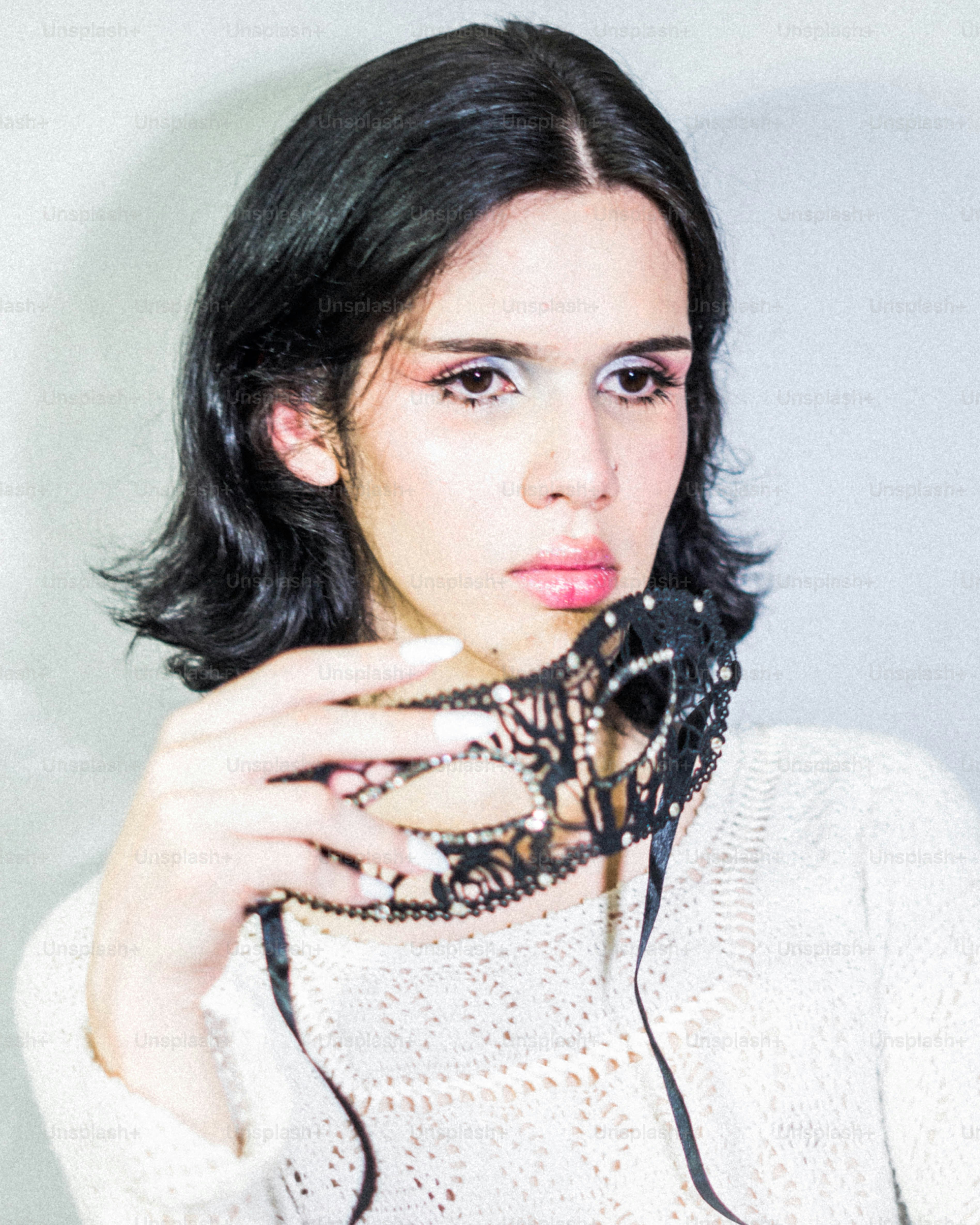 Person holding a black lace mask with rhinestones.