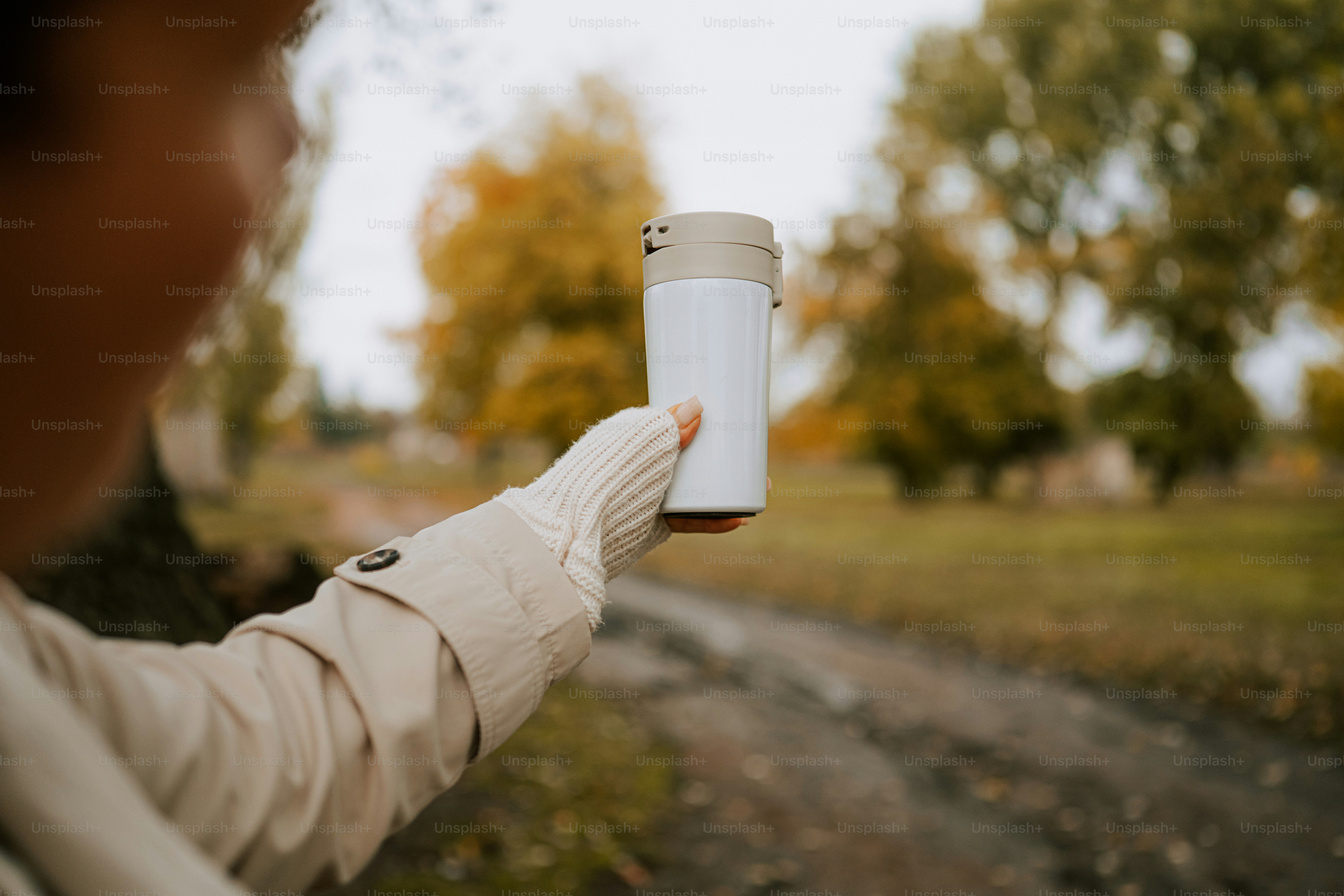 Personne tenant une tasse de voyage blanche à l’extérieur en automne.