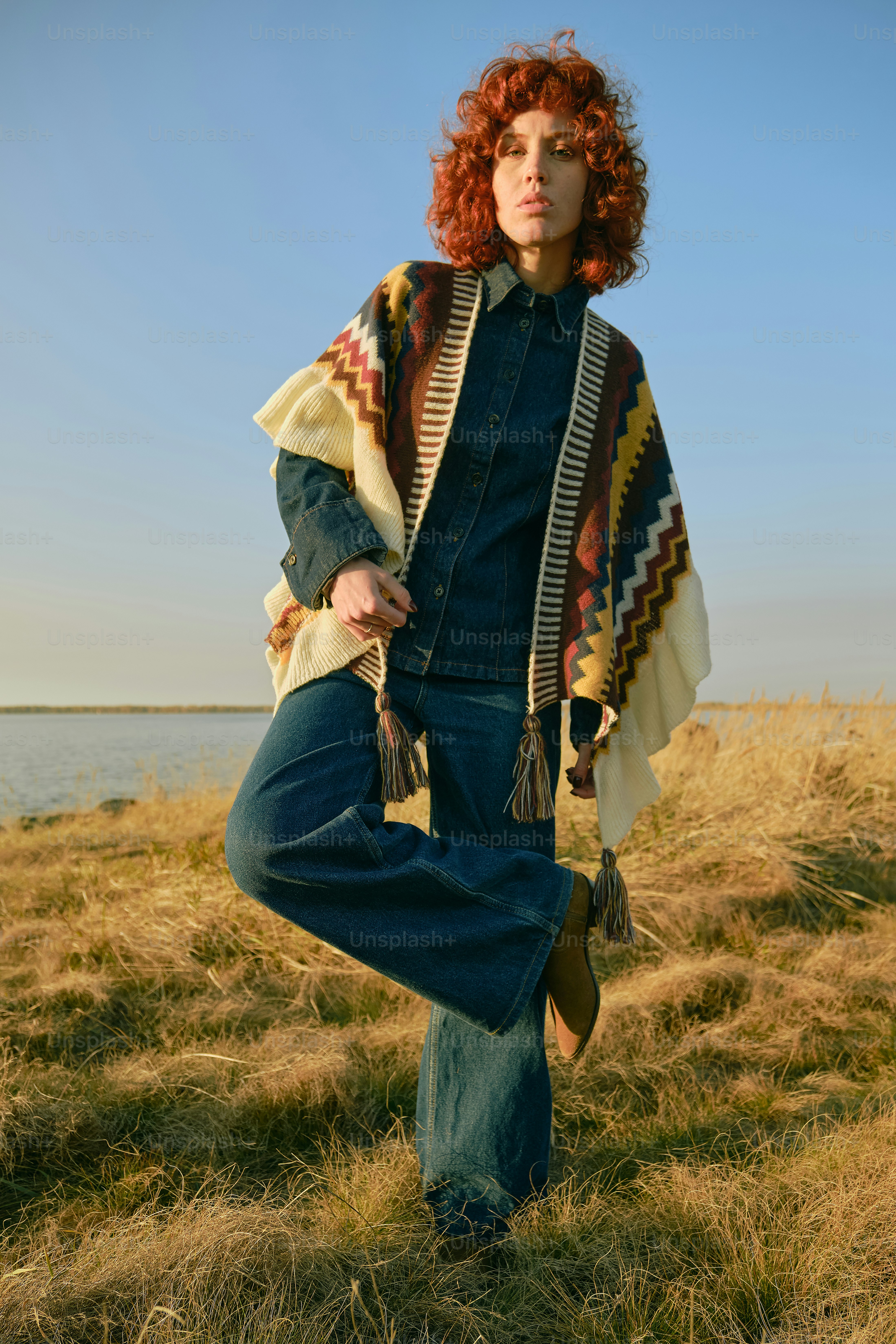 Frau in gemustertem Poncho und Jeans steht auf dem Feld