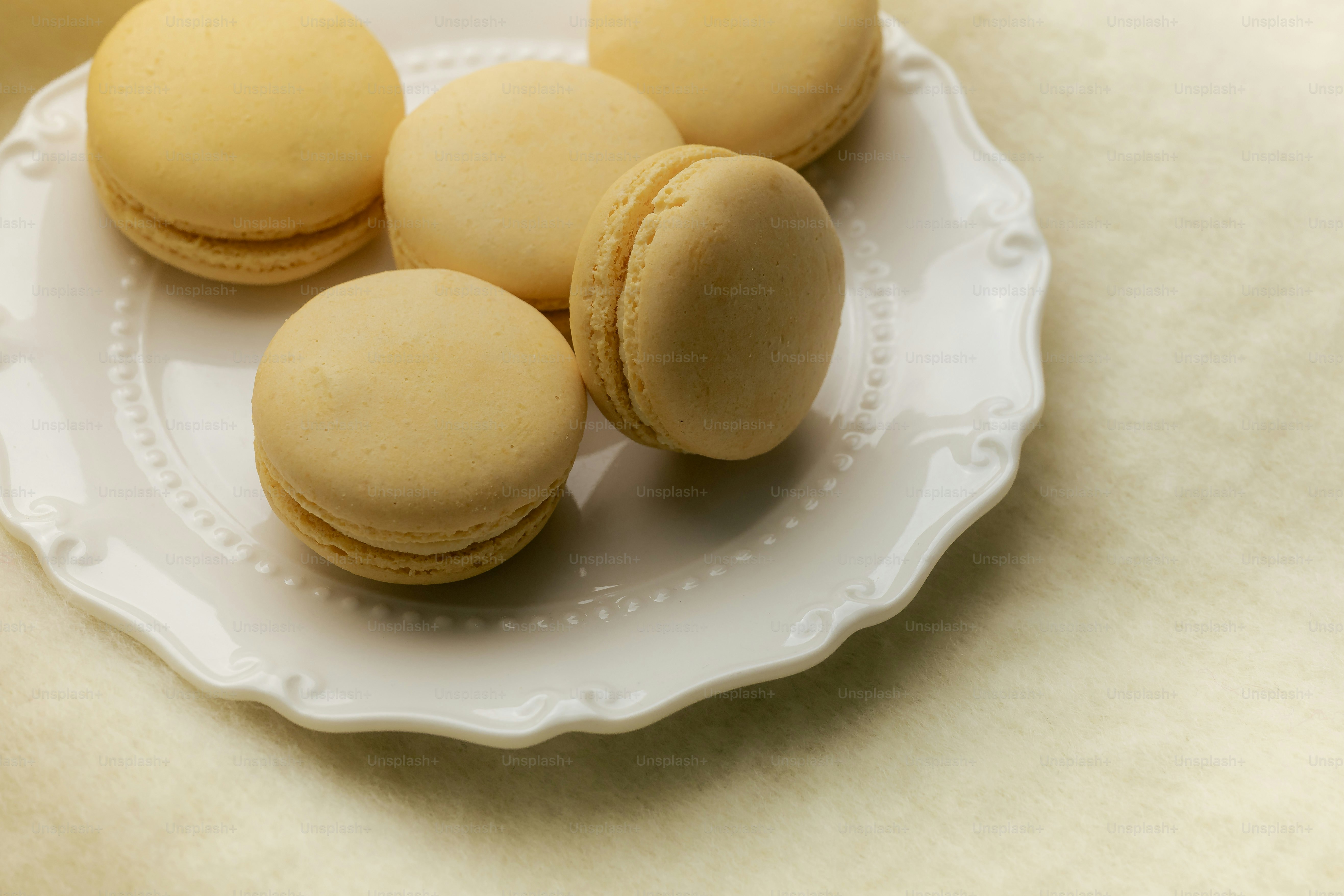 Five light brown macarons on a white plate