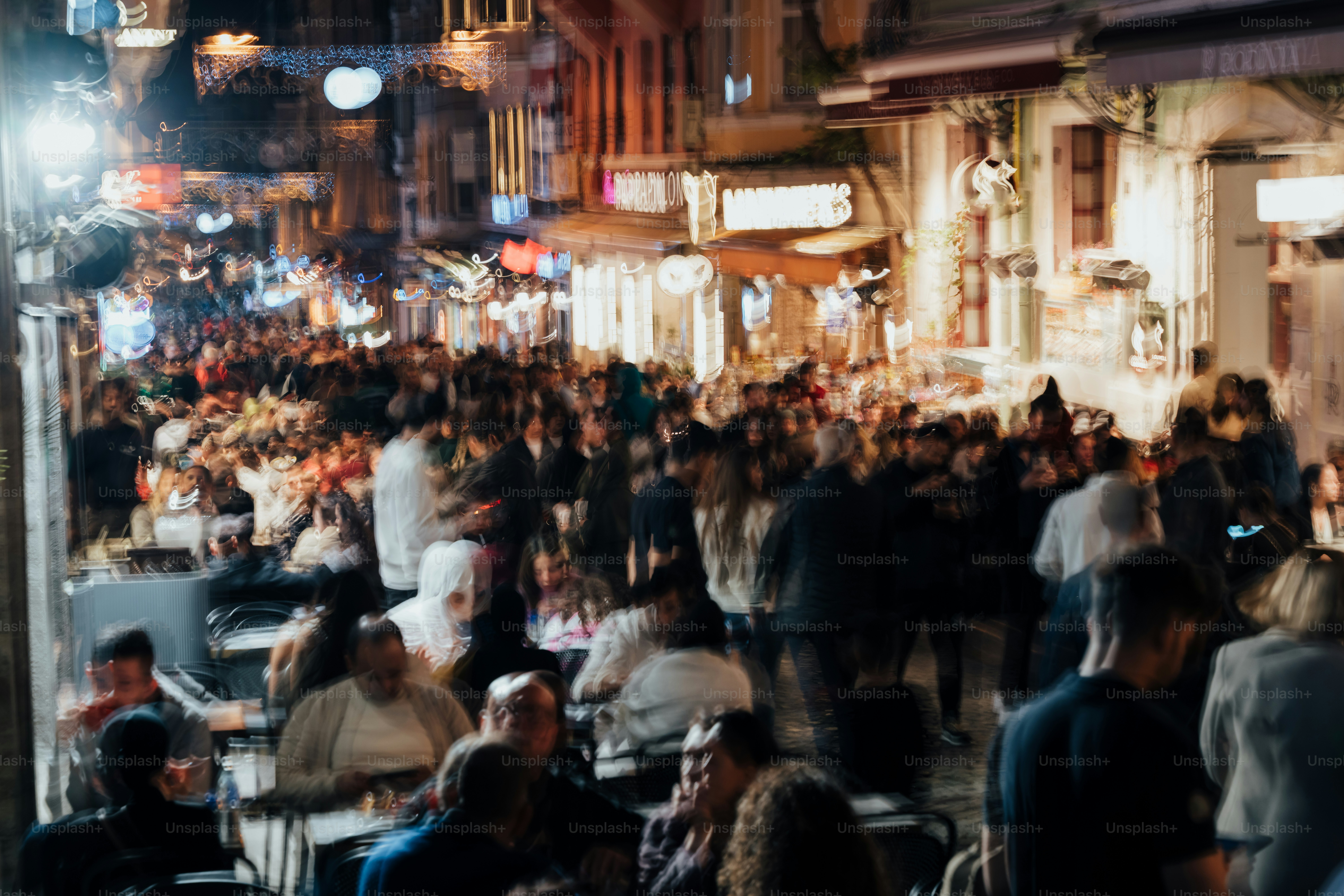 Crowded street with people dining at outdoor cafes at night.
