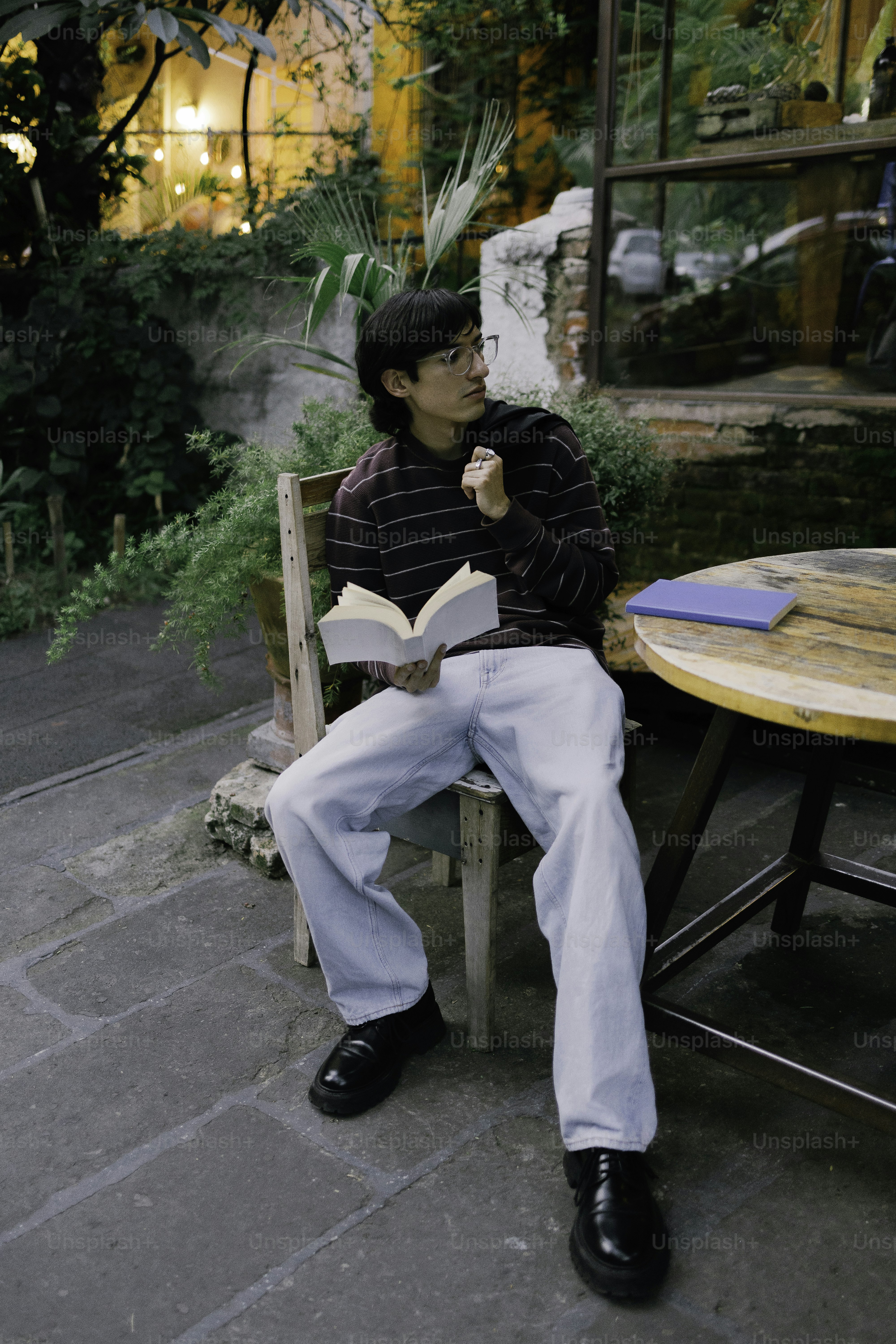 Young man reading a book outdoors at a cafe.