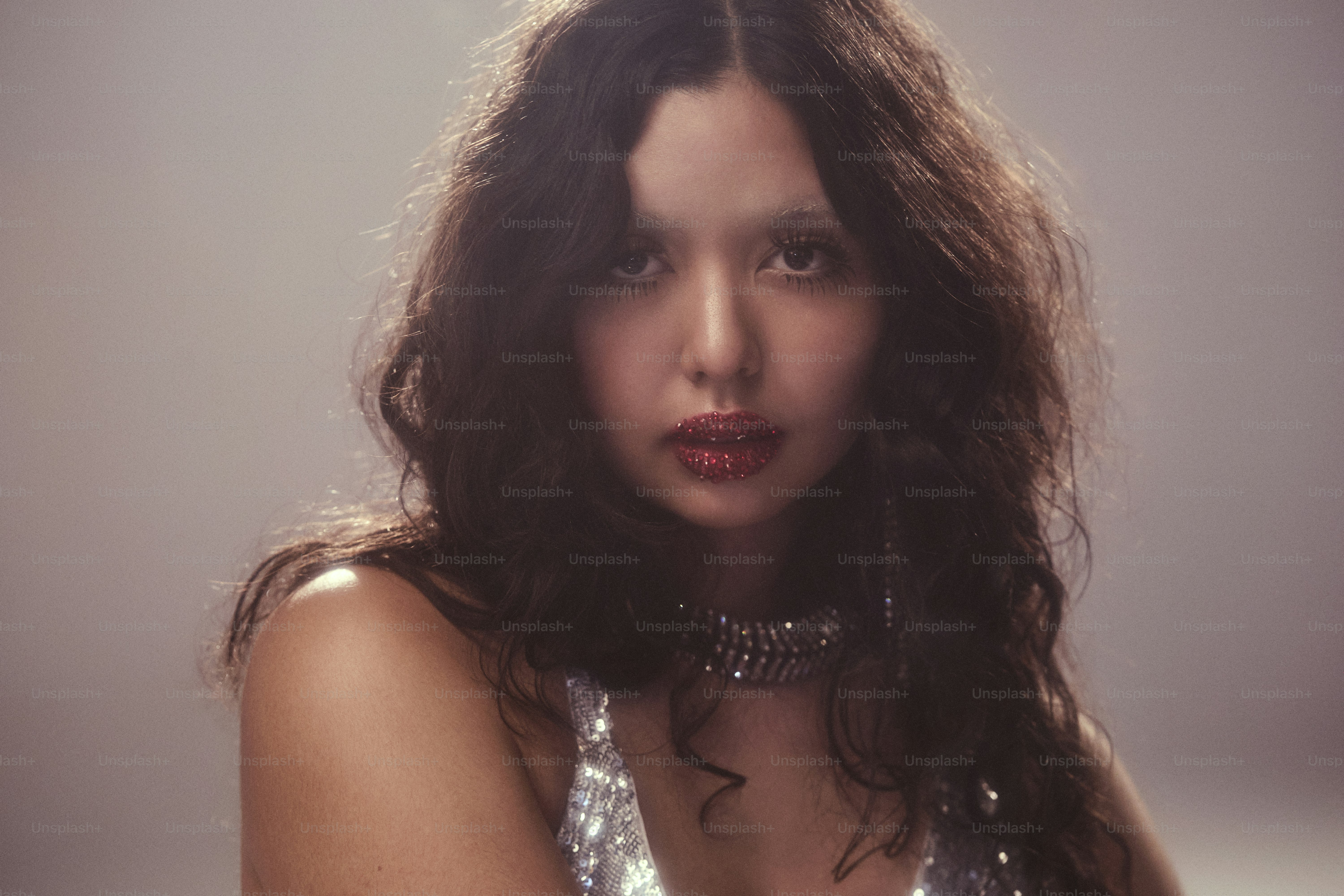 Une femme aux cheveux ondulés foncés et au collier scintillant.