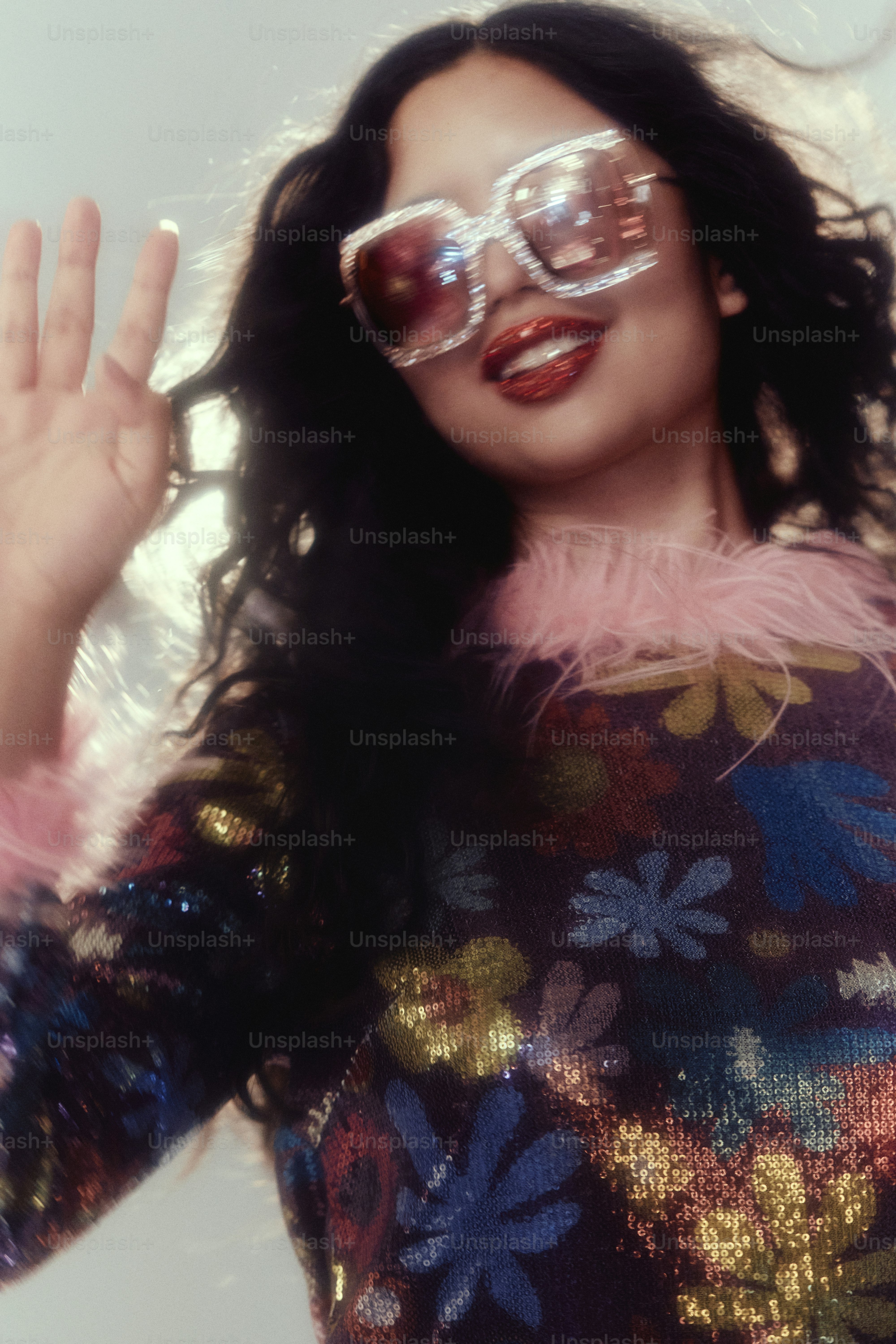 Woman with dark curly hair and sunglasses waves sunglasses