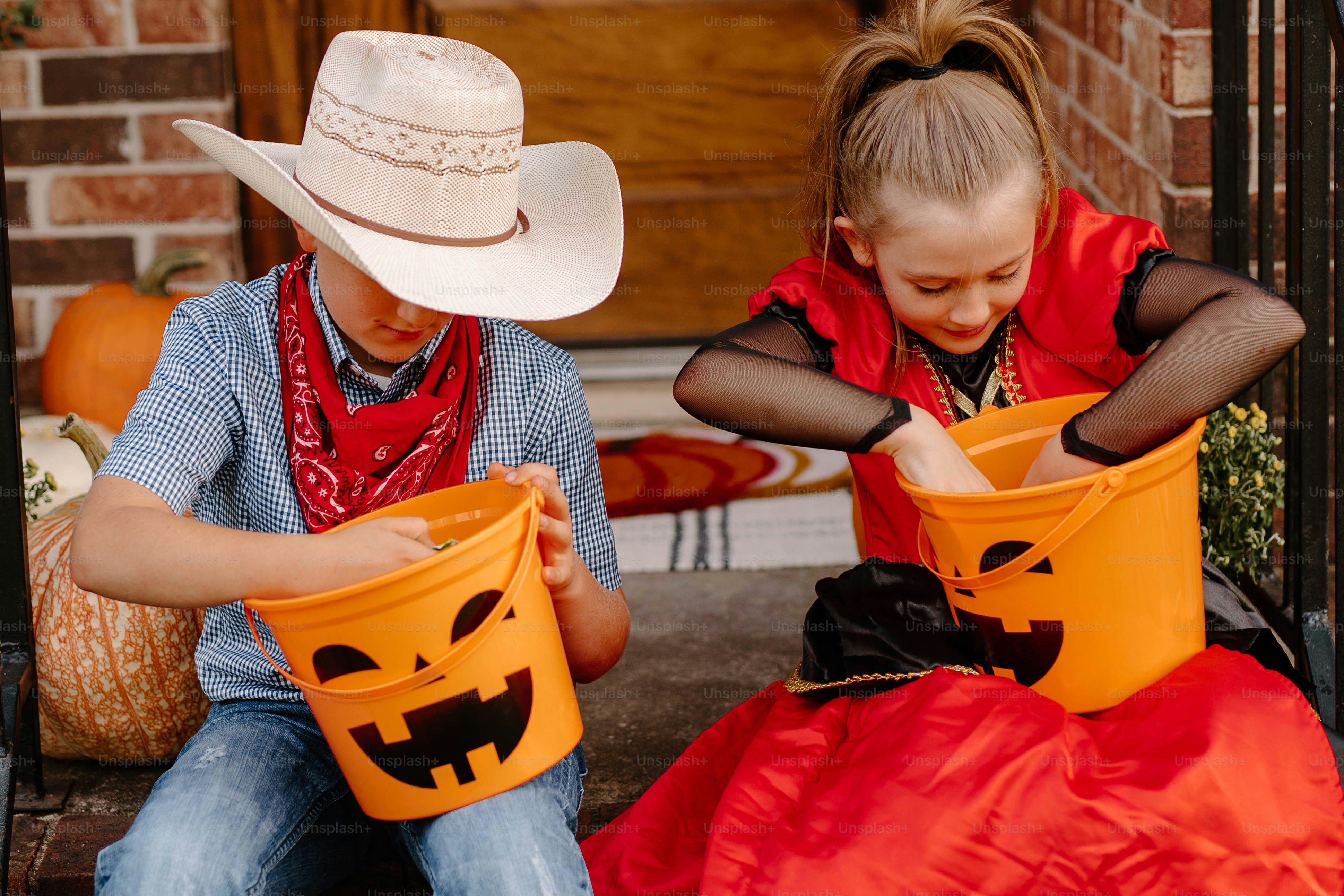 Two children in costumes collecting candy in pumpkin buckets.