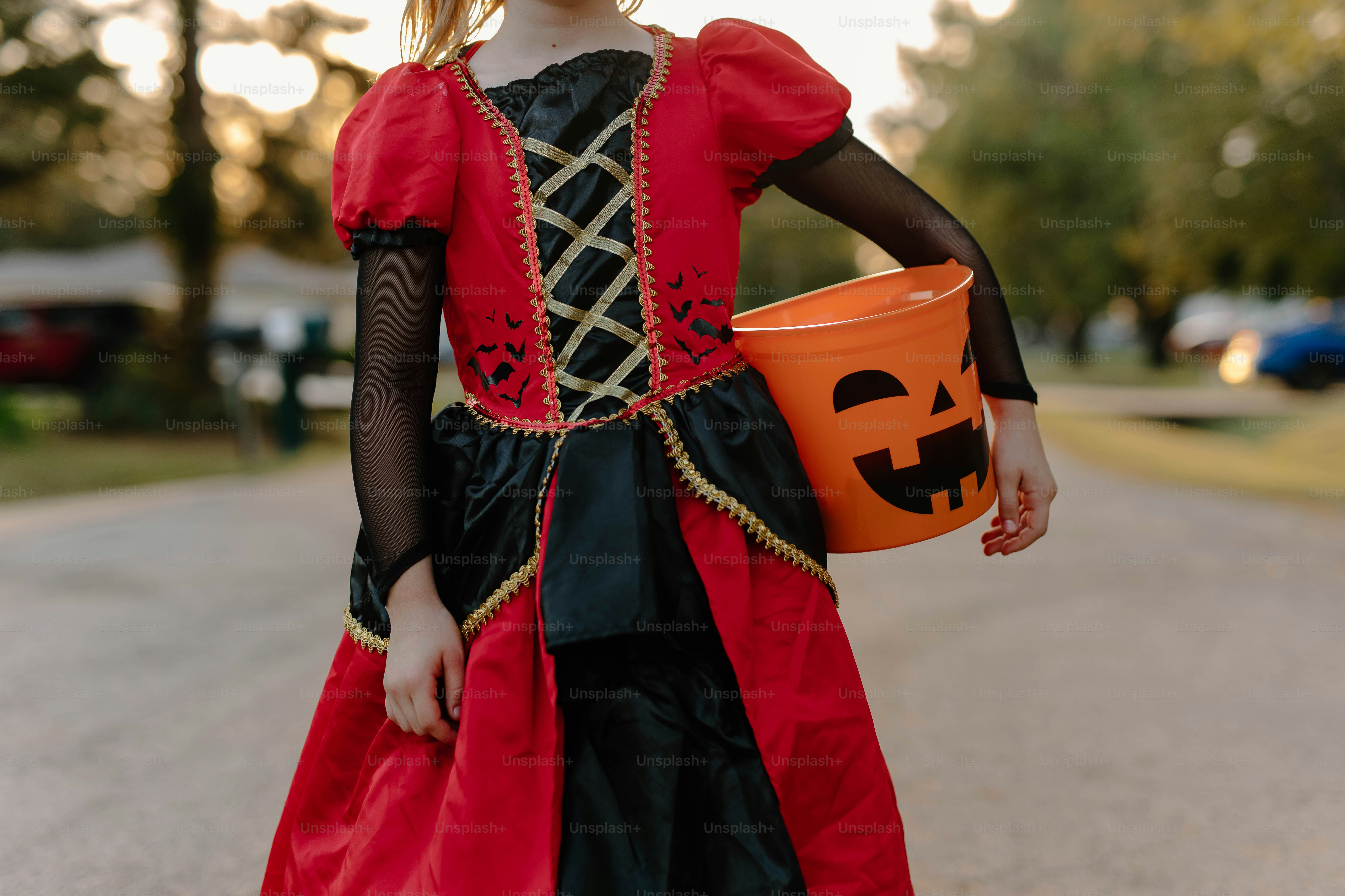 Child in costume holding a jack-o'-lantern bucket