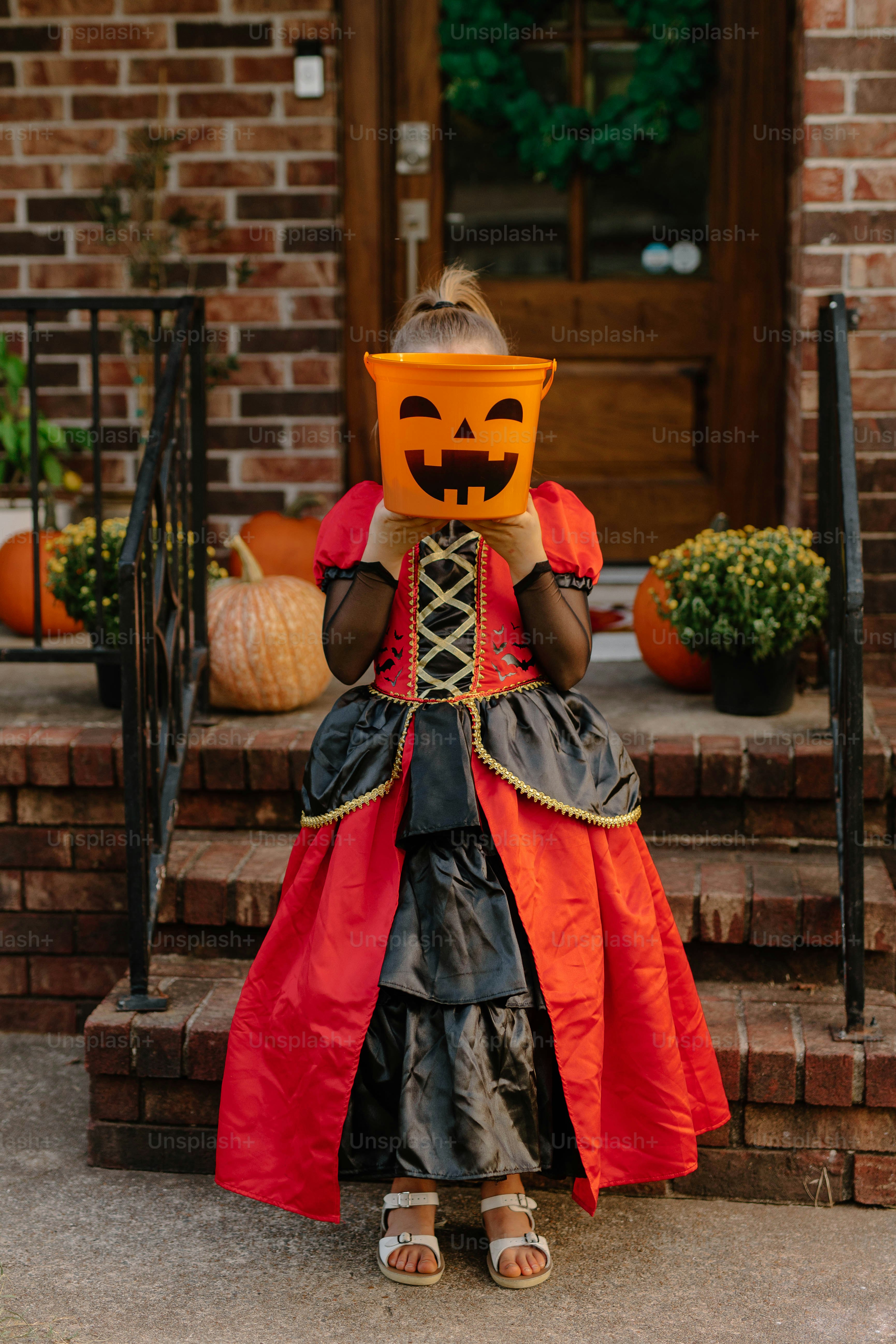 Child in costume holds pumpkin bucket at door