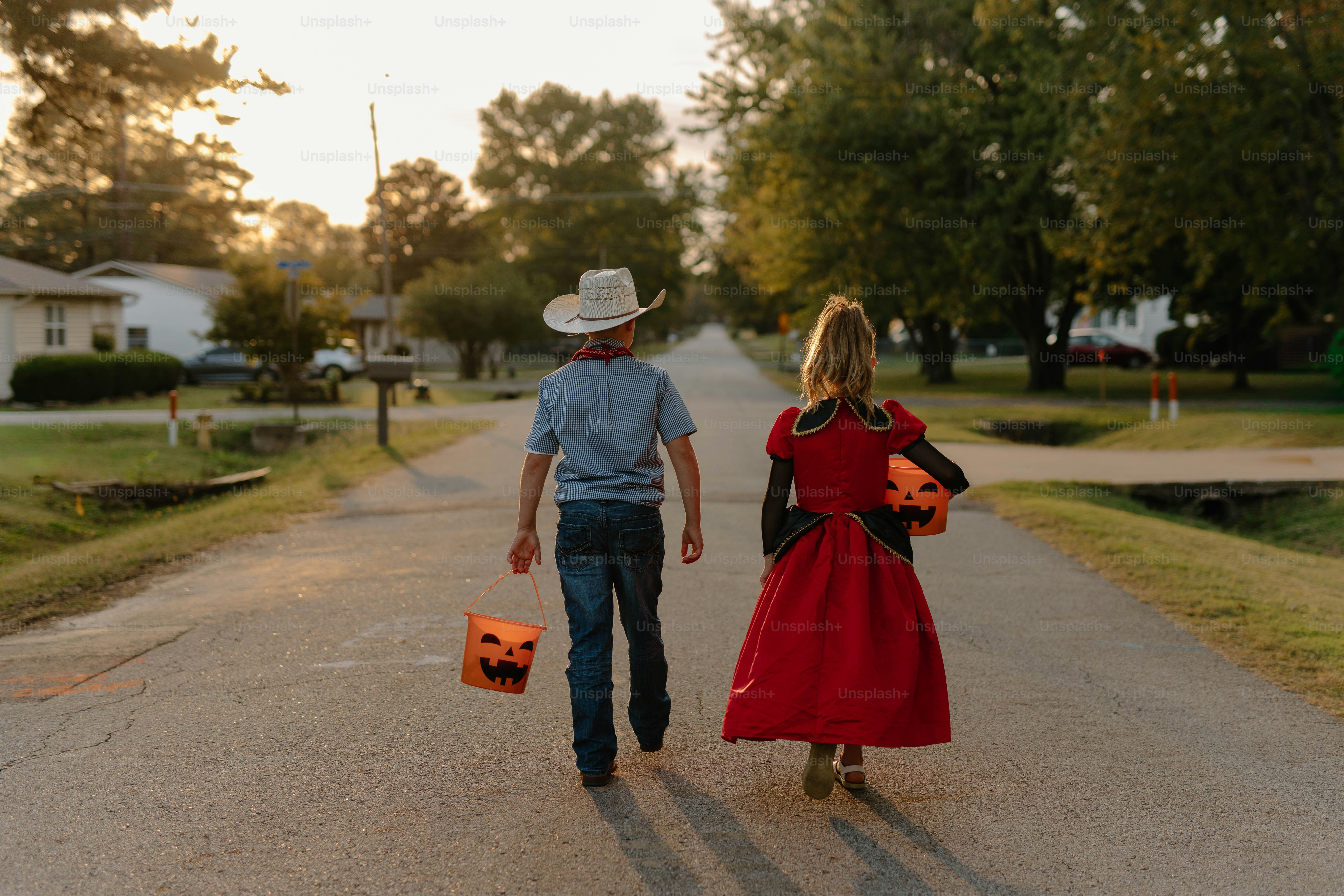 Two children in costumes walking down a street.