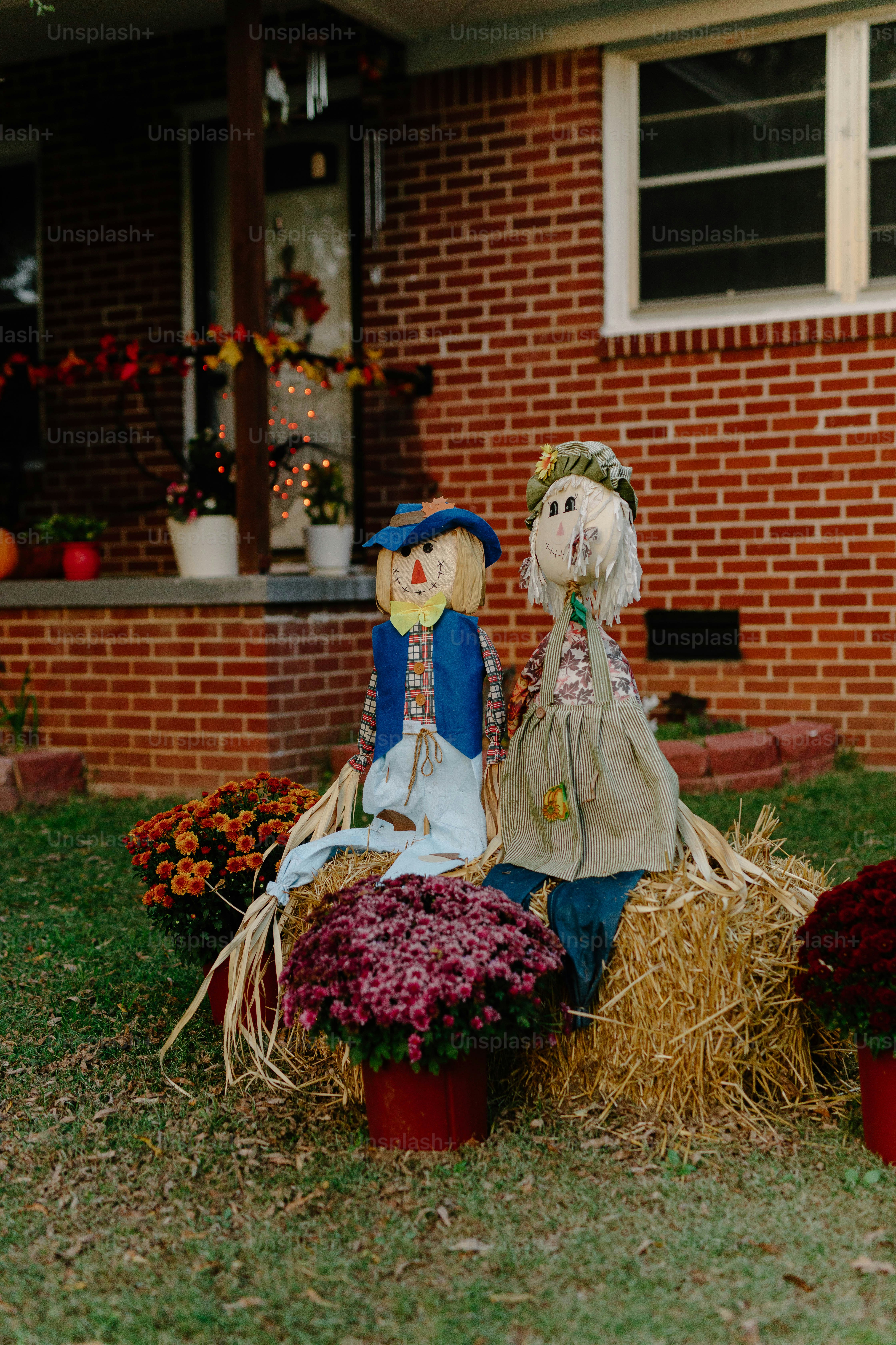 Two scarecrows sit on hay bales with mums