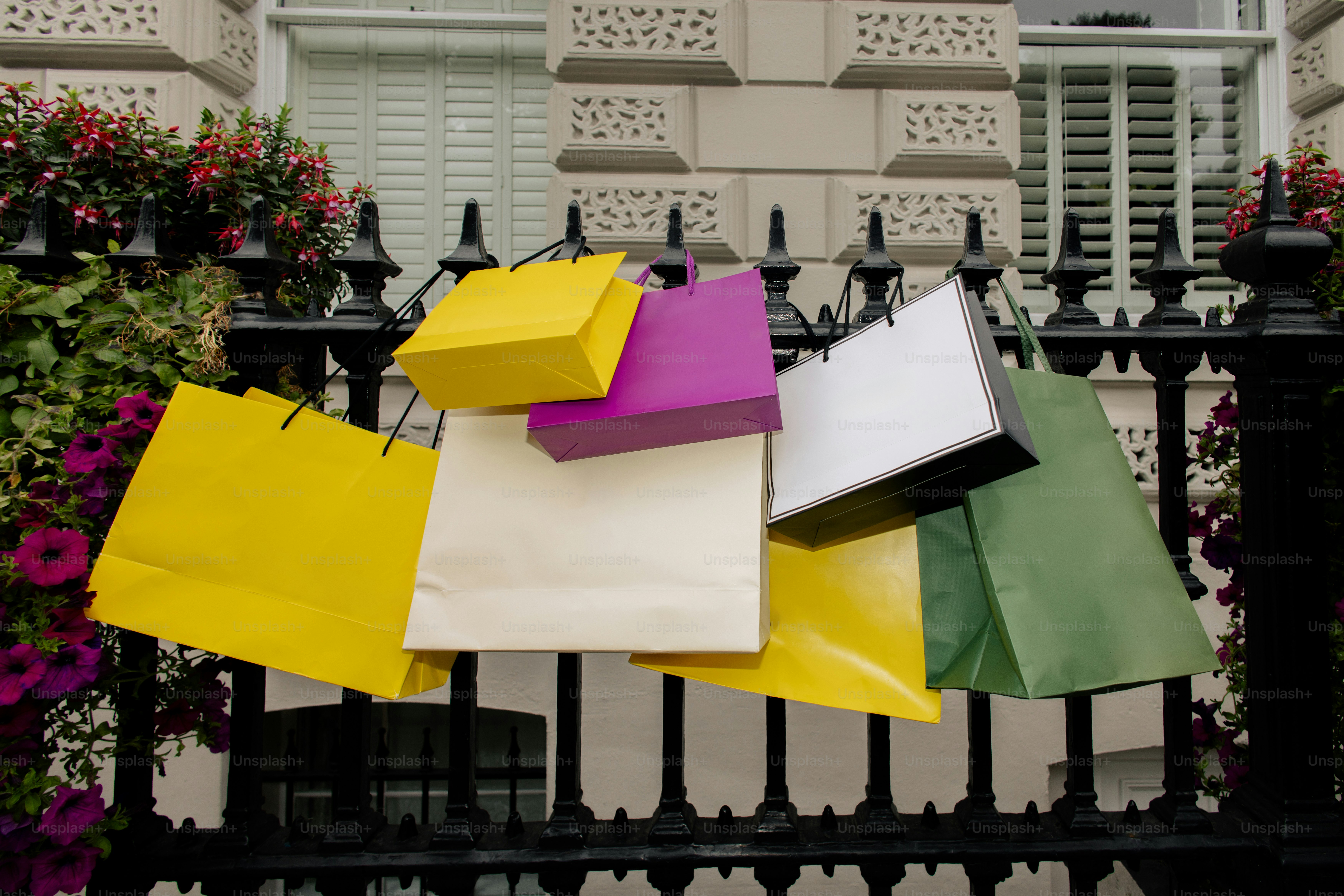 Colorful shopping bags hanging on a black fence.