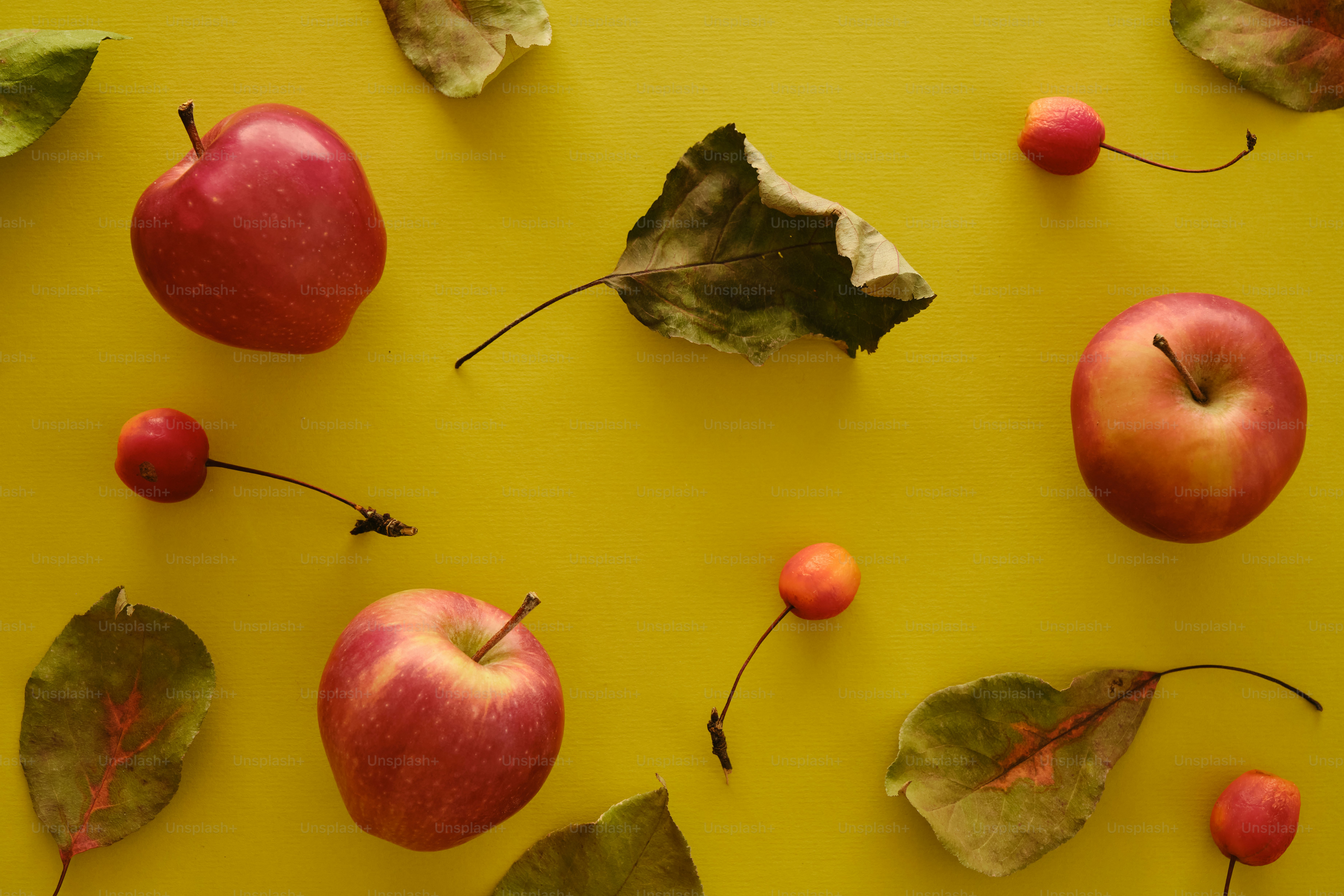 Red apples and autumn leaves on yellow background