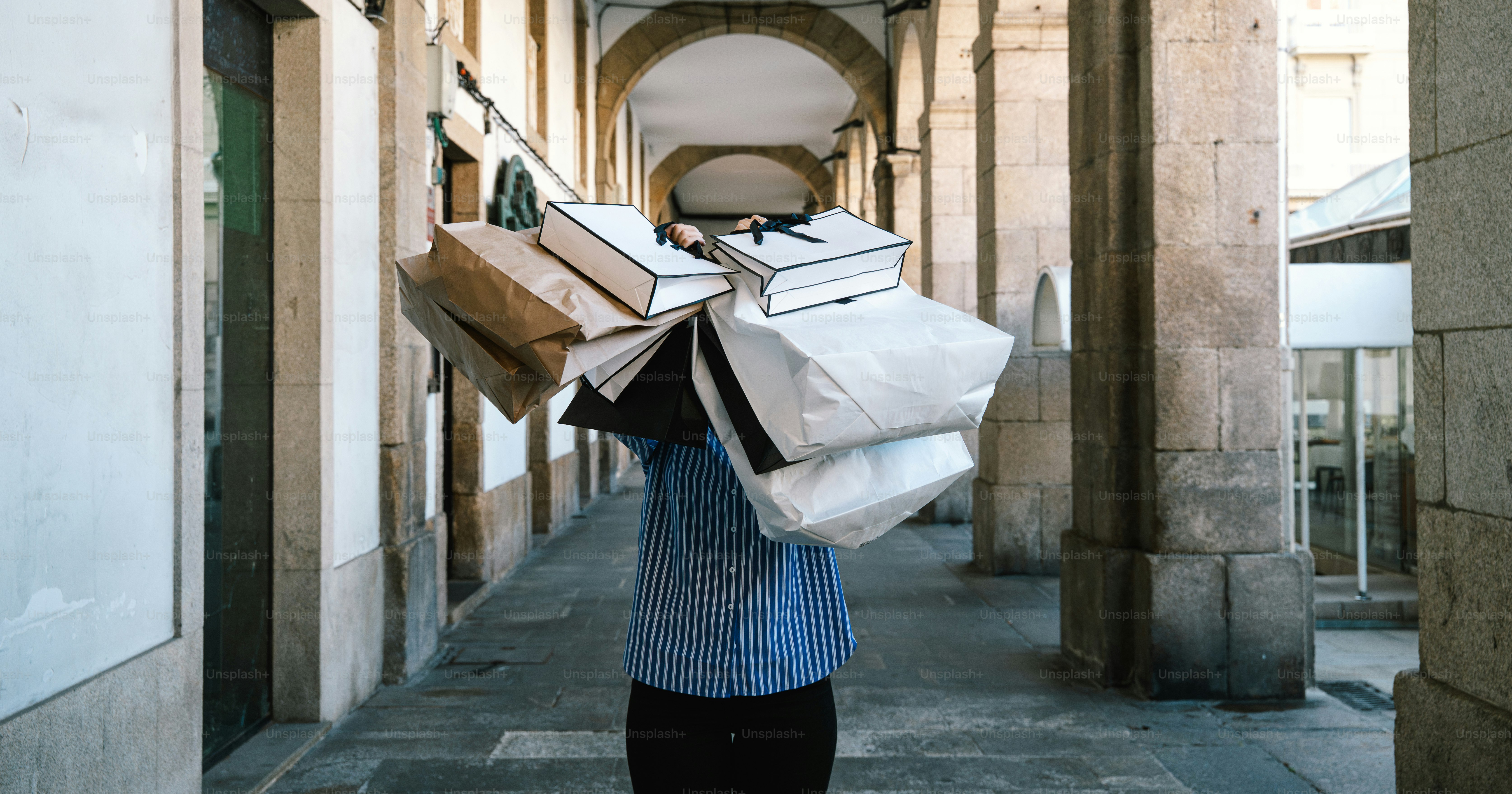Person carrying many shopping bags down an arcade.