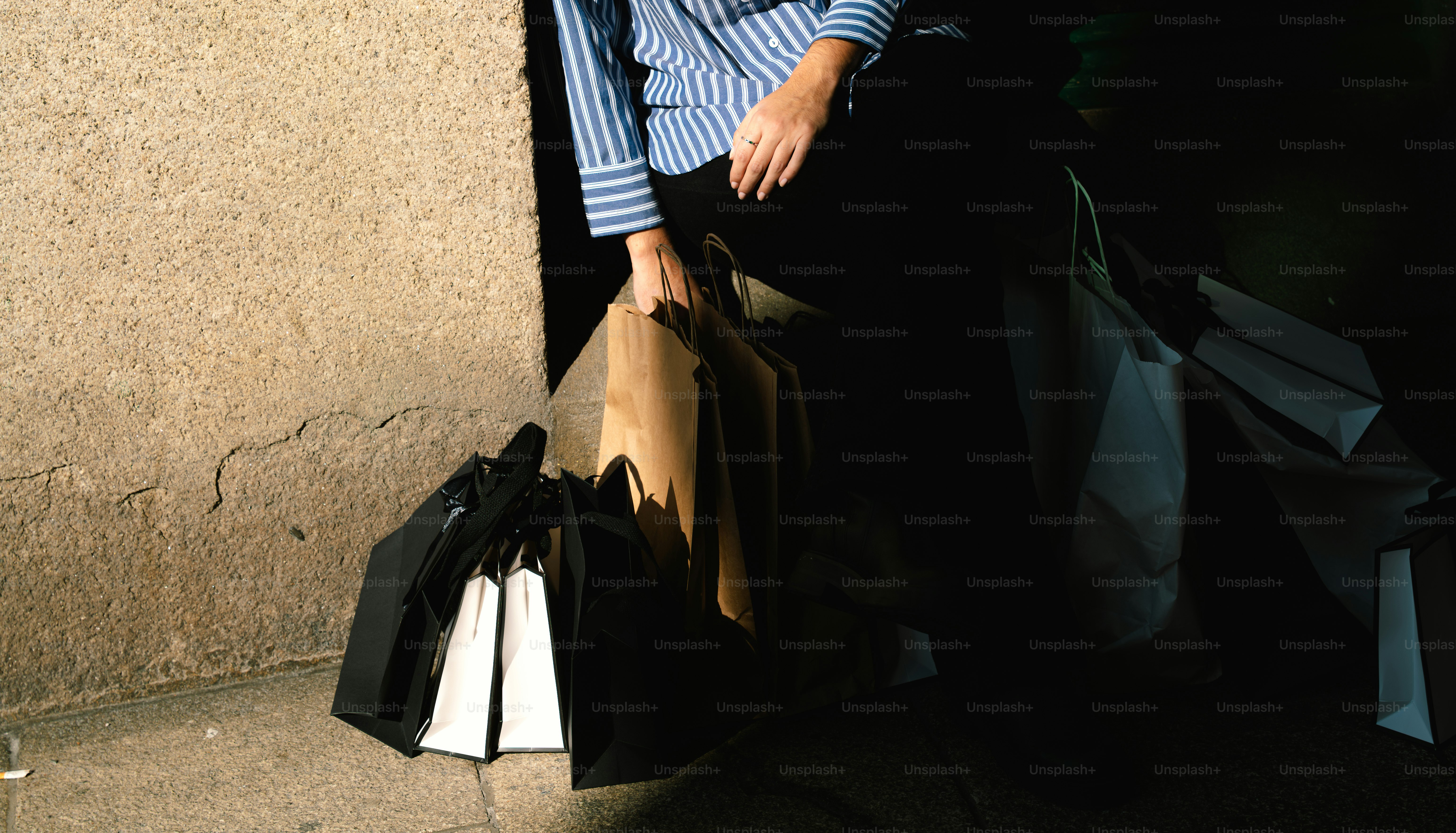 Persona sosteniendo bolsas de compras cerca de un muro de piedra