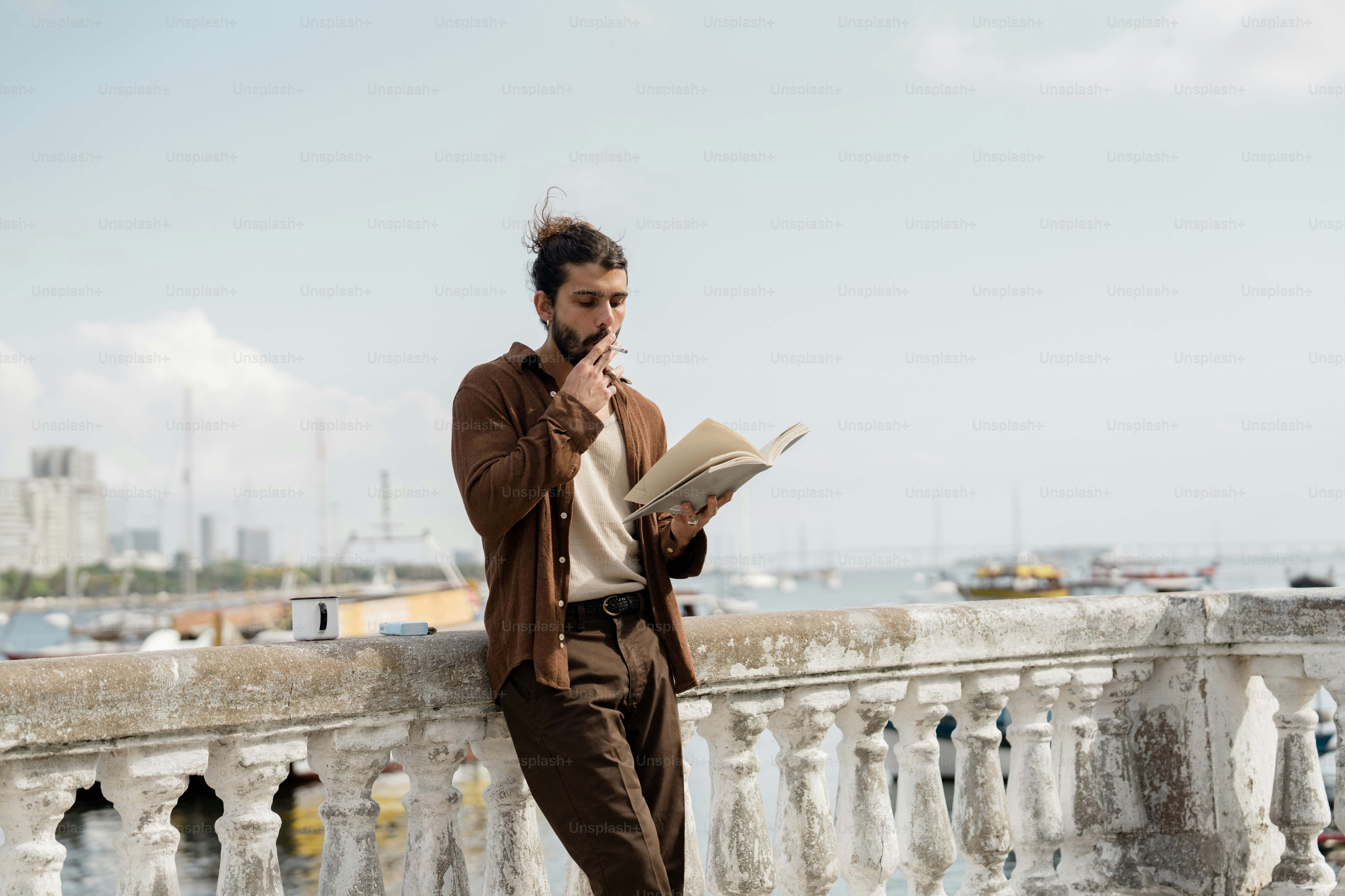 Man in brown jacket reading book by railing