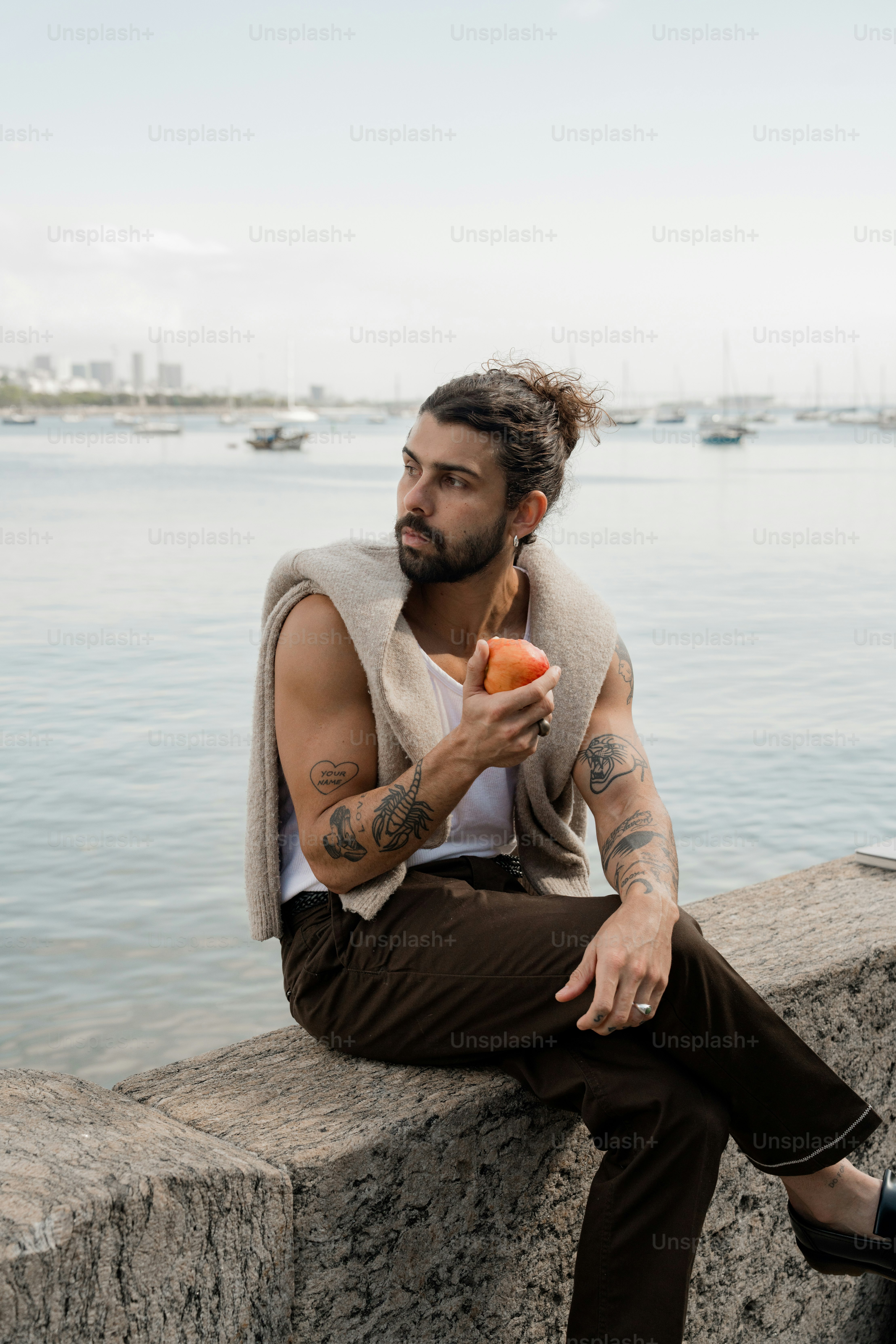 Mann mit Tattoos, der eine Orange am Wasser hält.