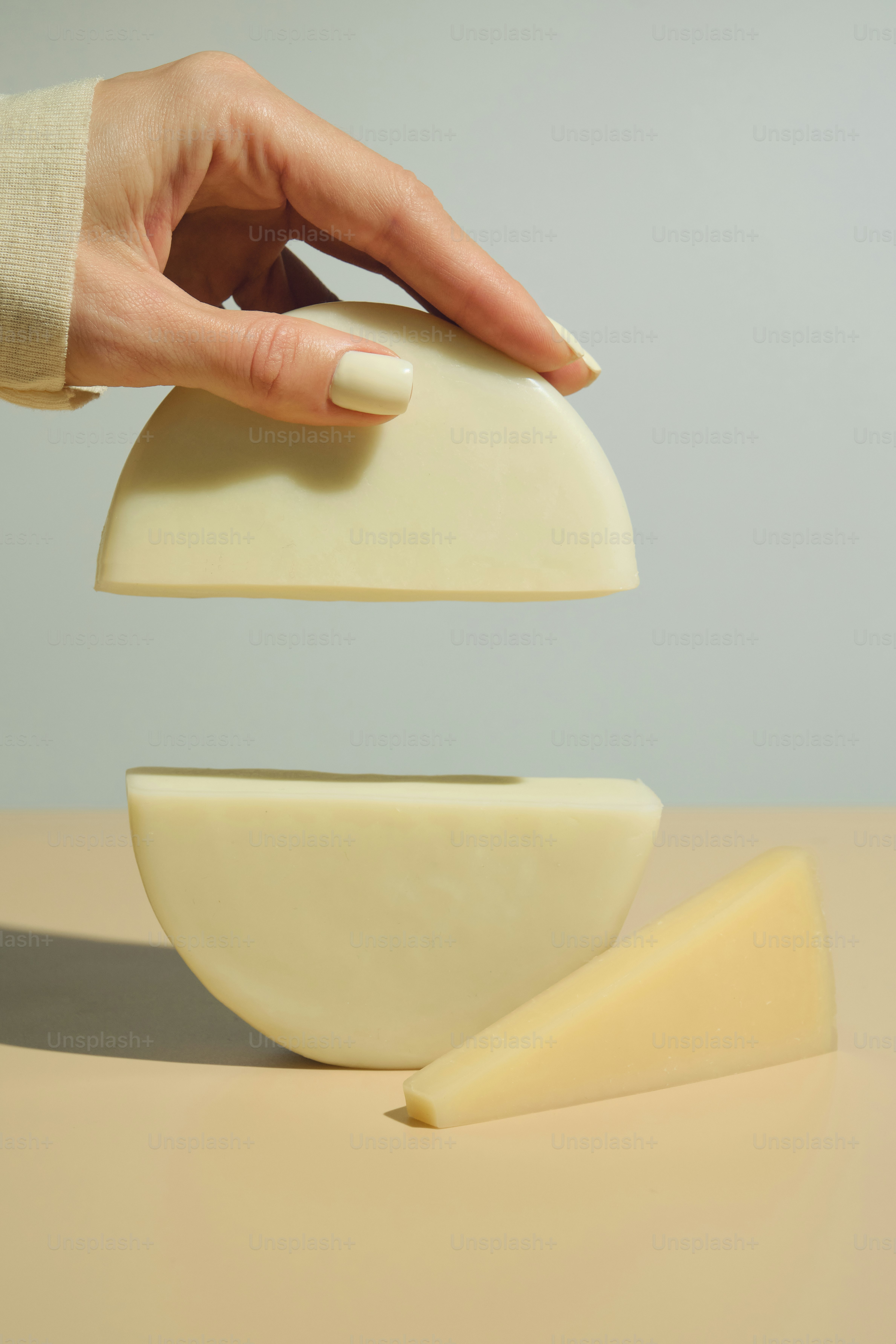 Hand hält geometrische Käsescheiben vor neutralem Hintergrund