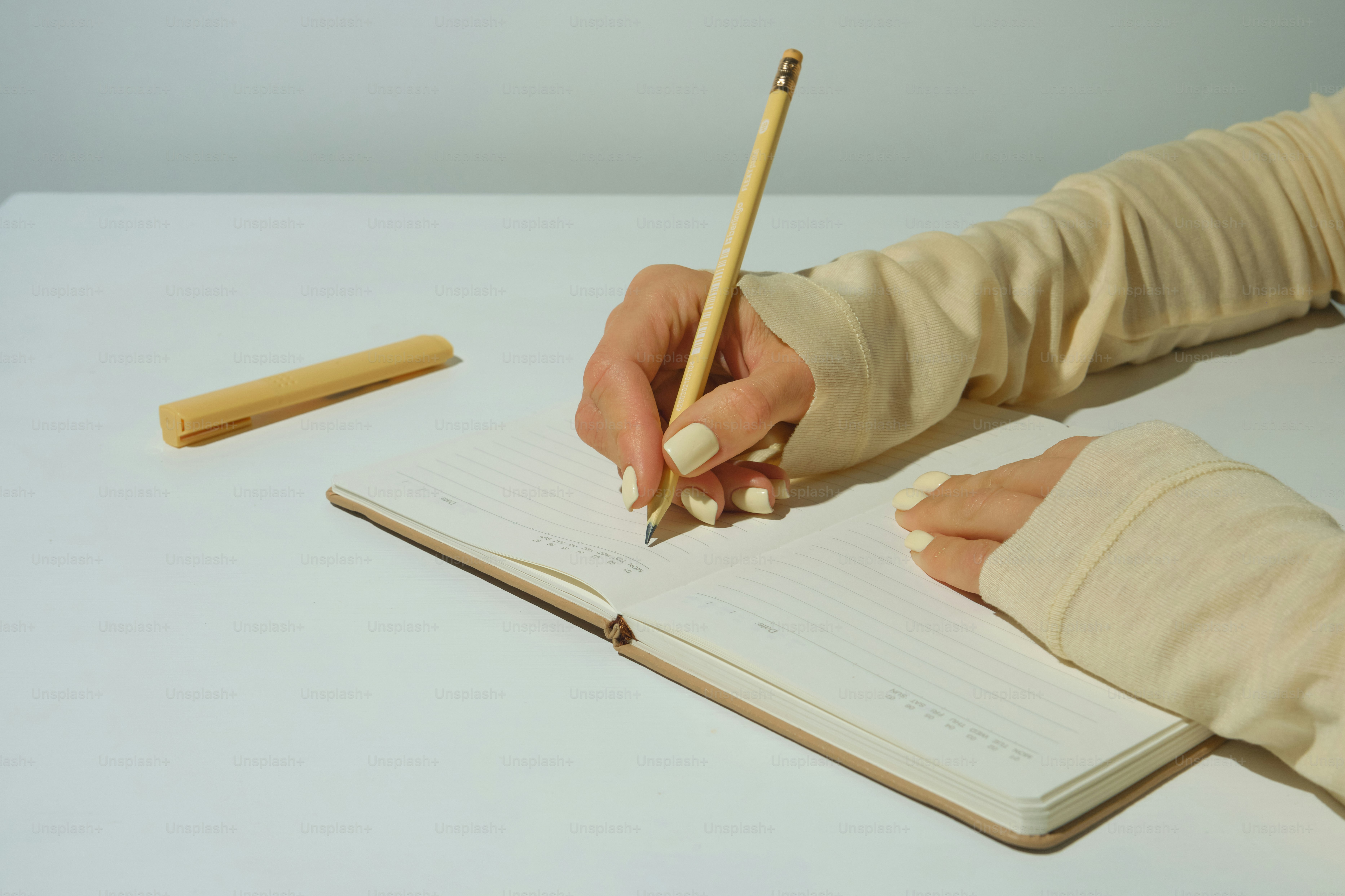 A person writing in a notebook with a pencil.