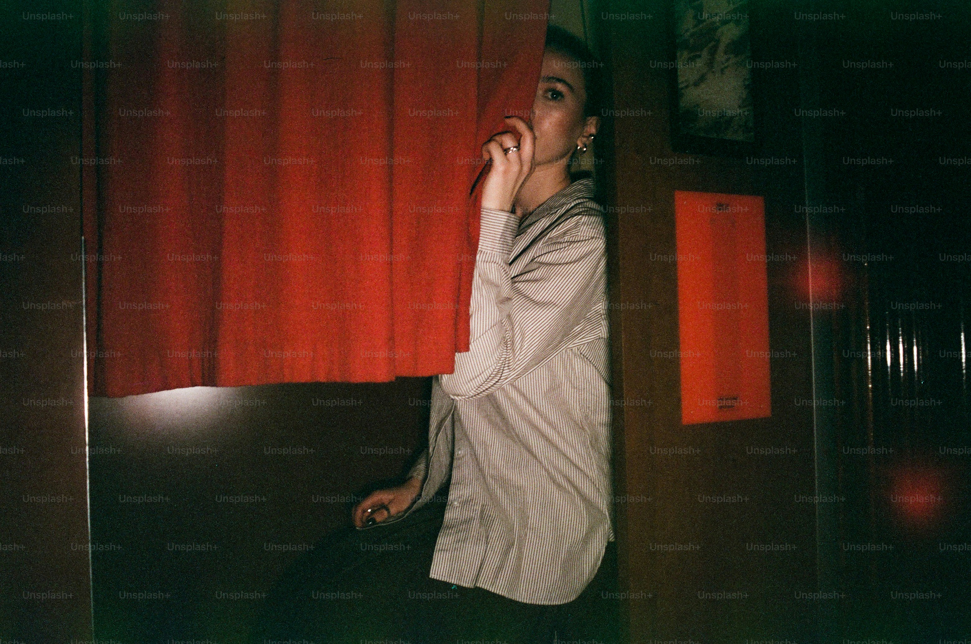 Woman peeking through red curtain in dimly lit room.