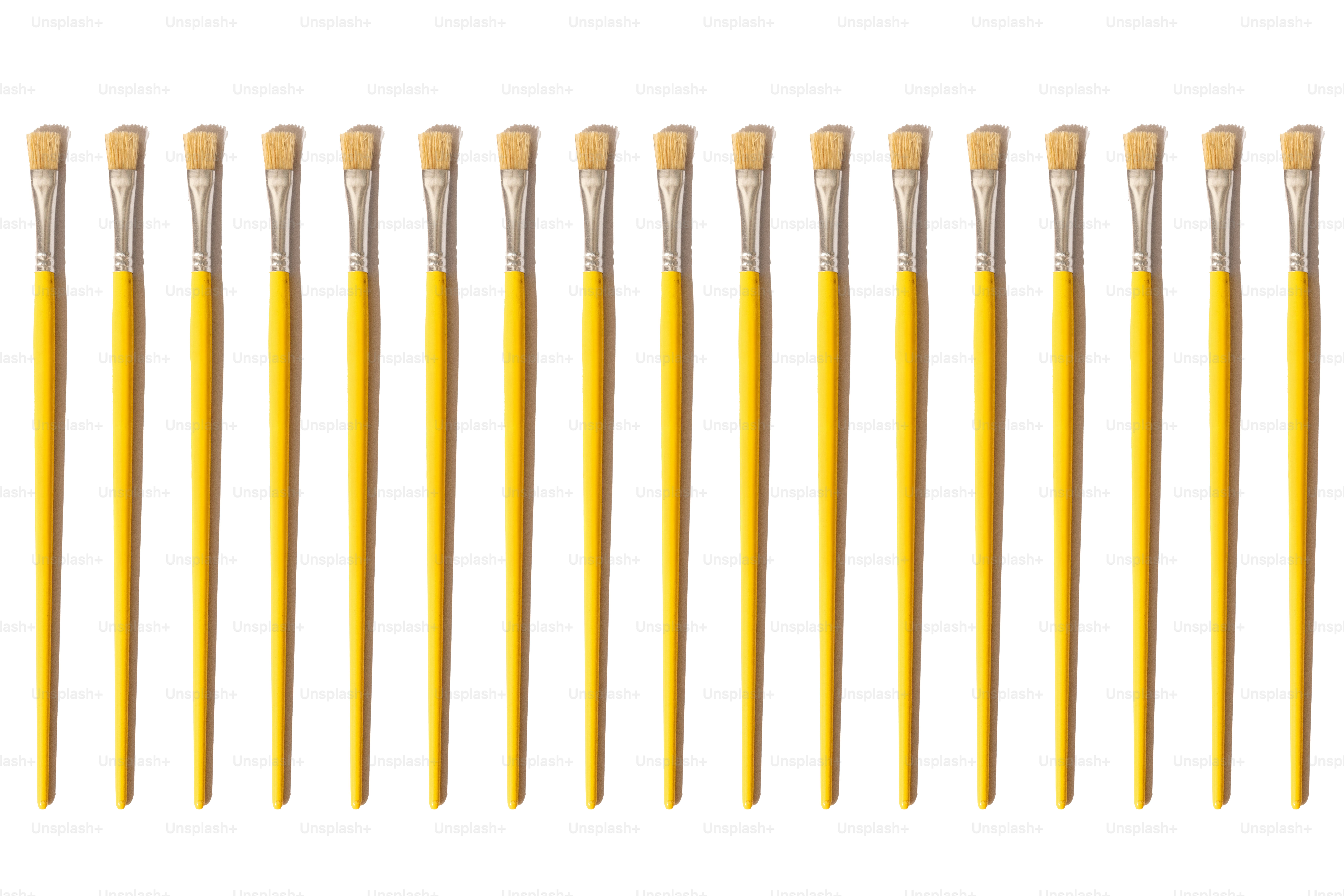 A row of yellow paintbrushes on white background