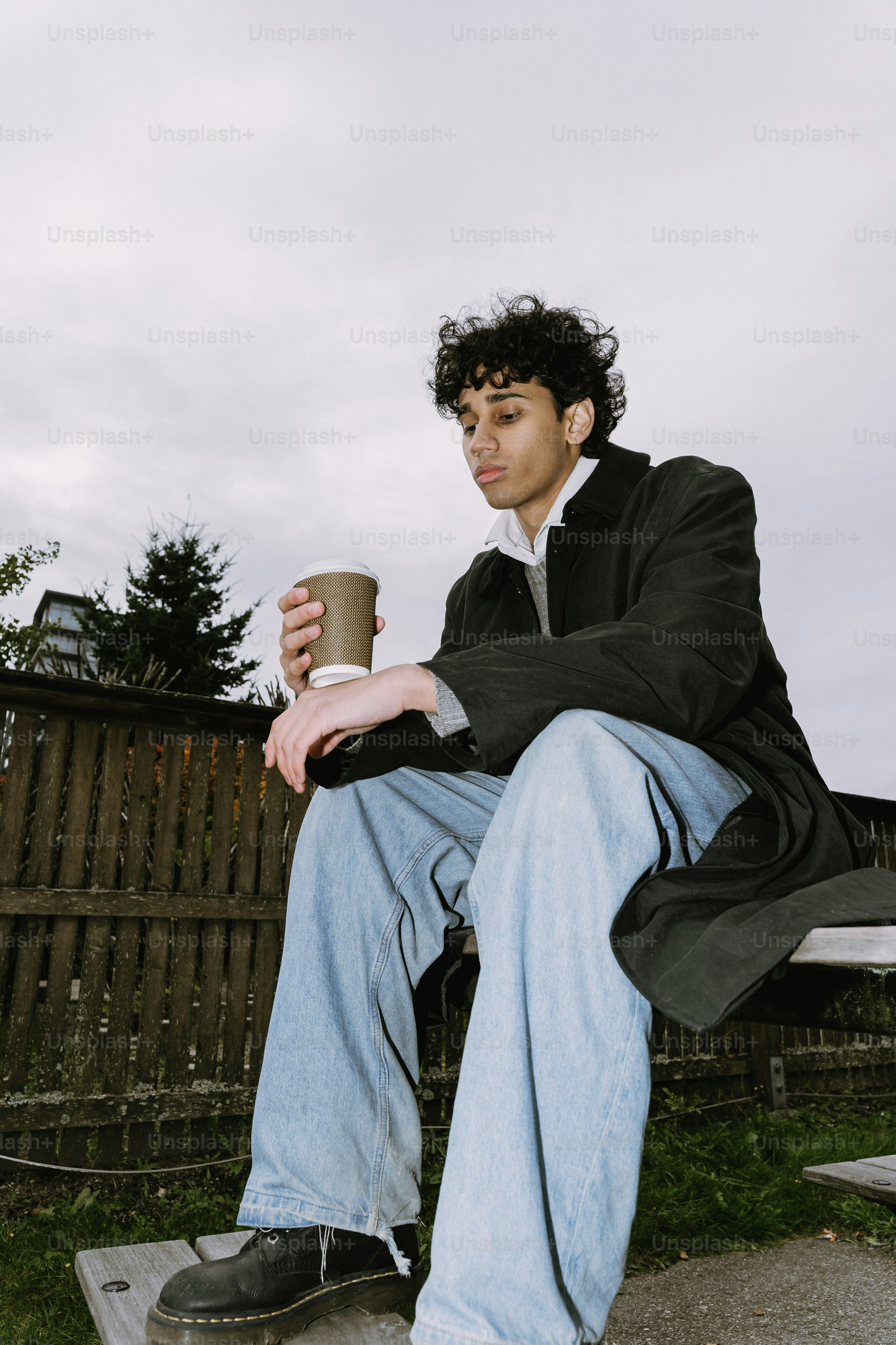 A young man with curly hair holds a coffee cup.