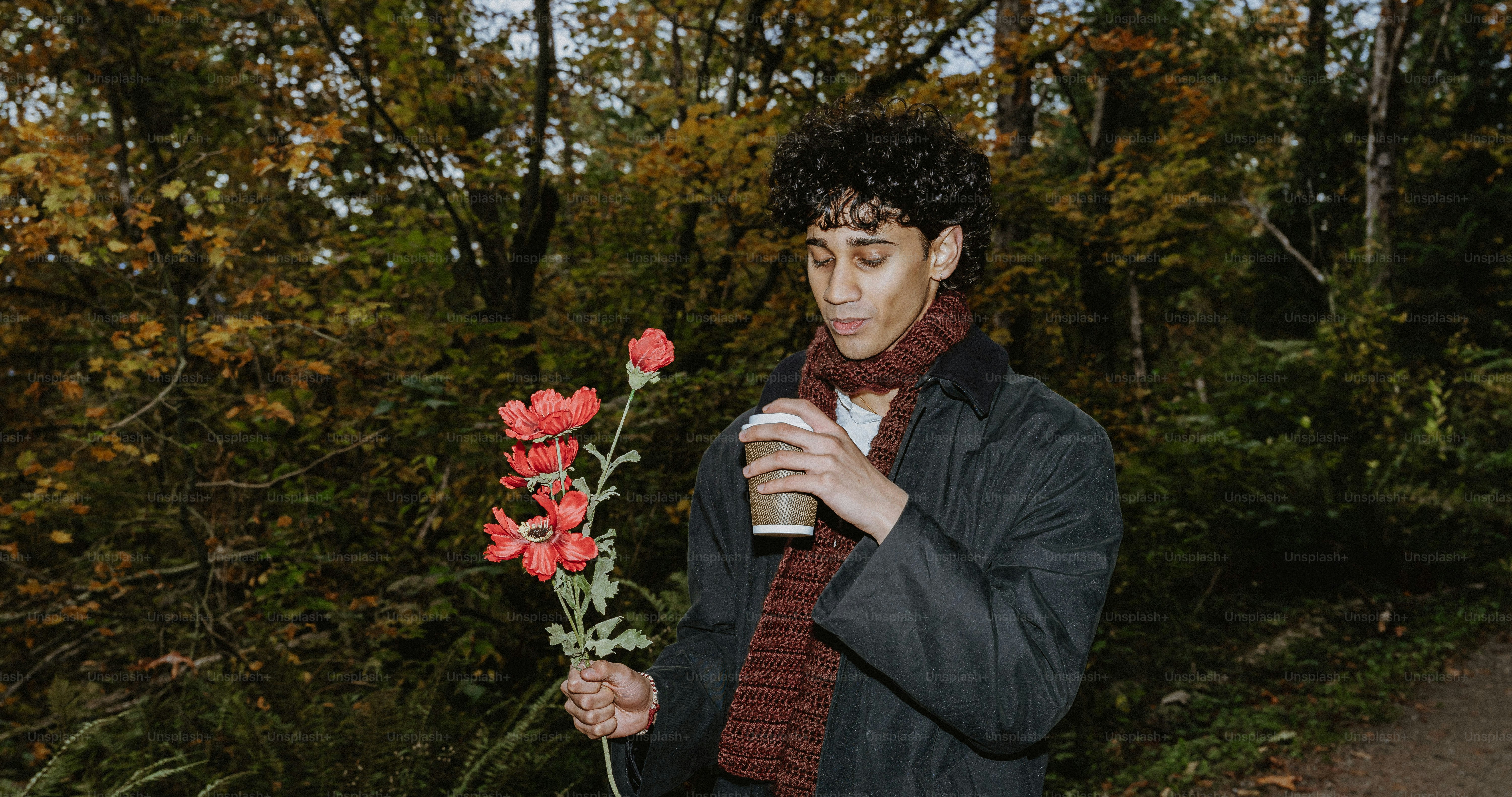 Person holding flowers and coffee in autumn park