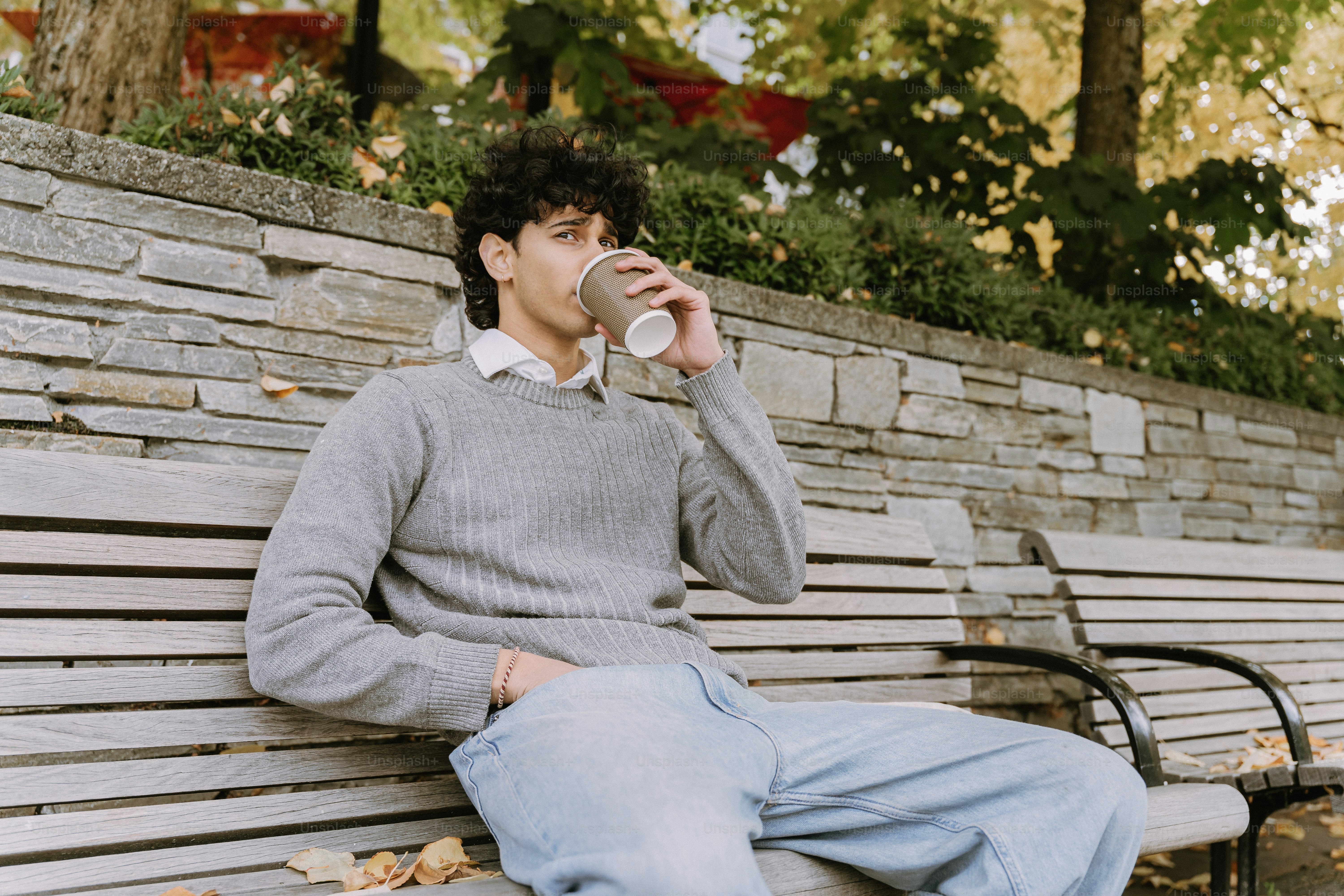Young man drinking coffee on a park bench.