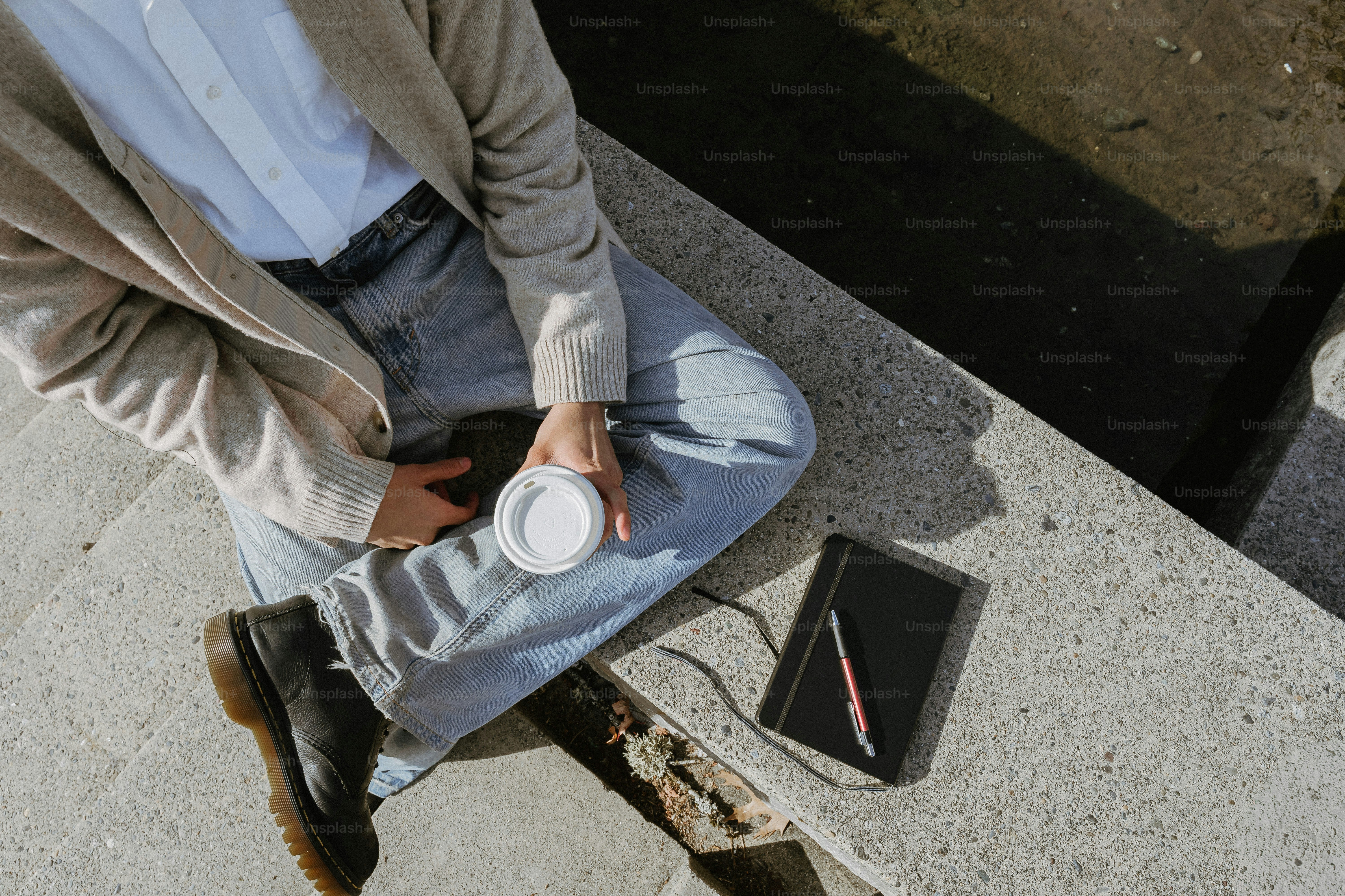 Person holding coffee cup with notebook and pen.