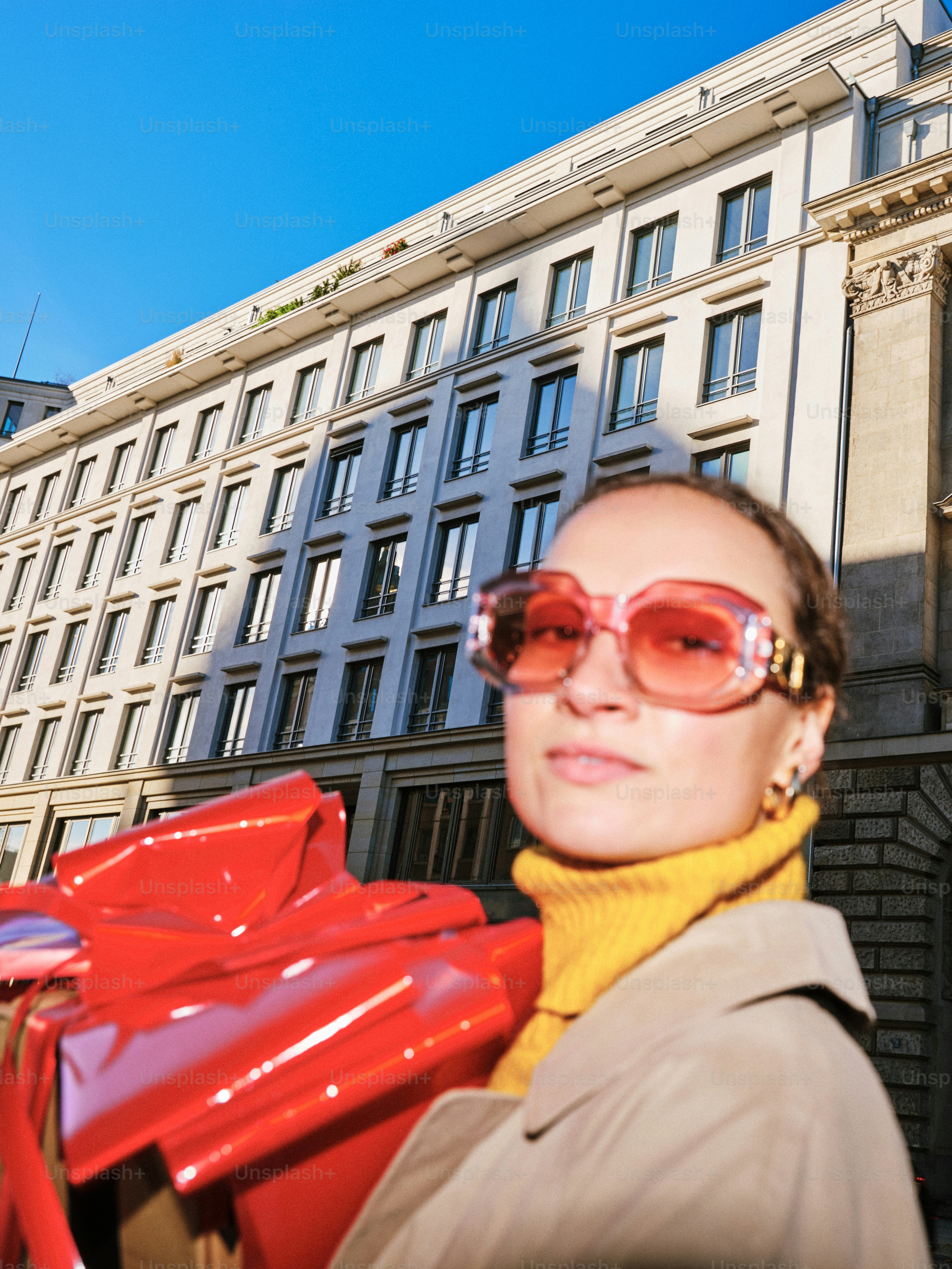 Woman in sunglasses holds large red gift box.