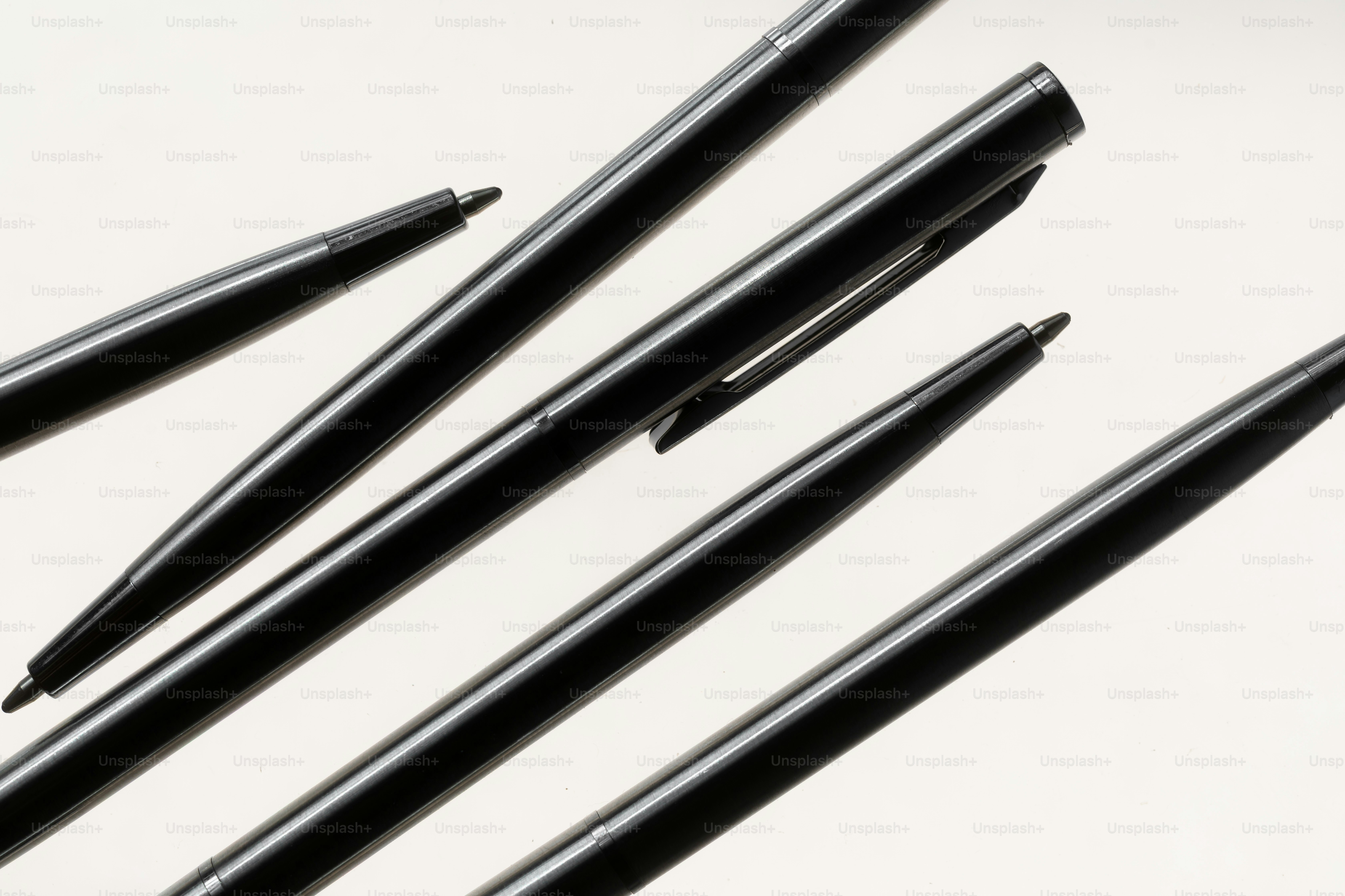 Several black pens arranged on a white surface.