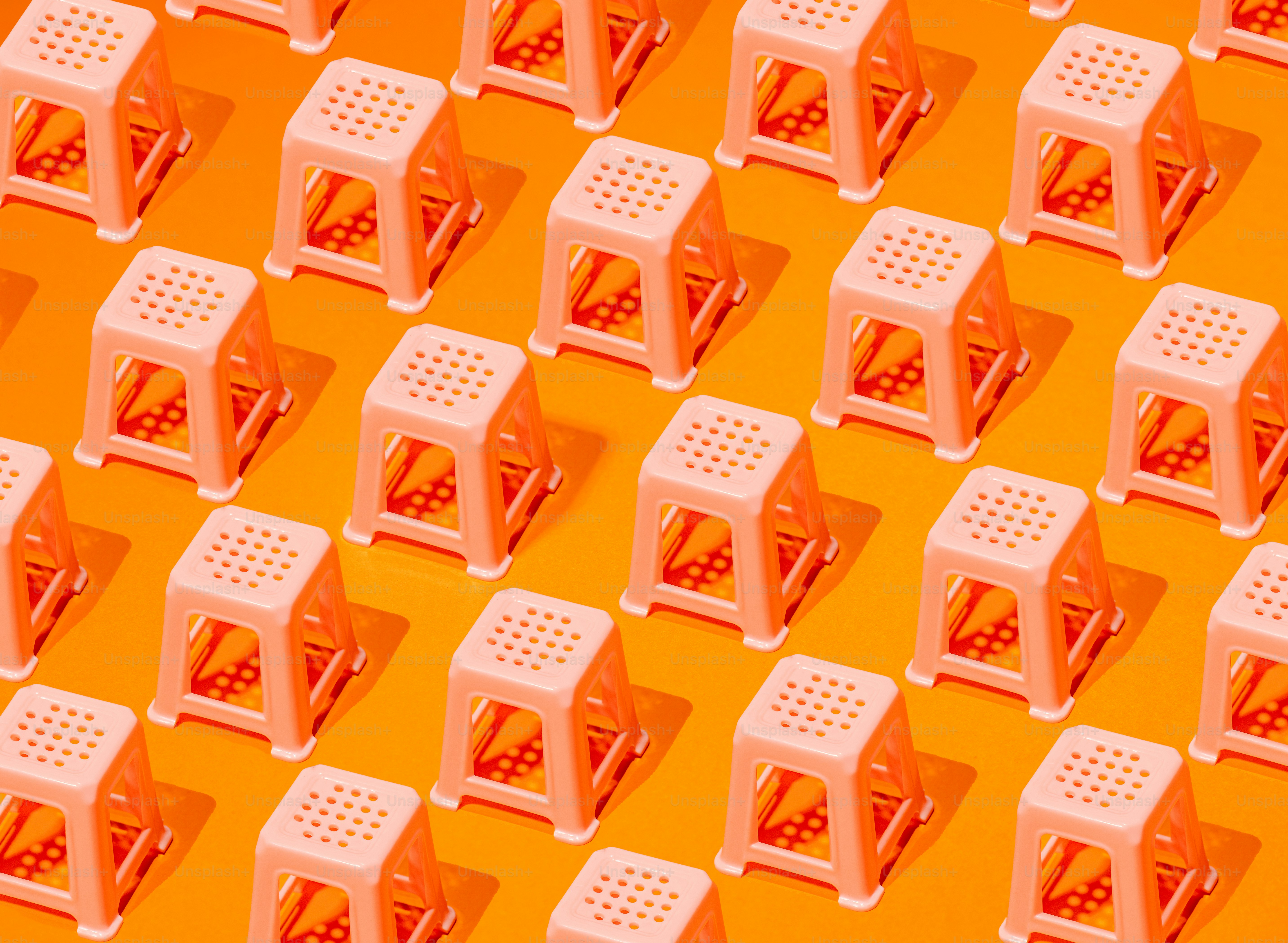 Muster aus kleinen rosa Hockern auf orangefarbenem Hintergrund