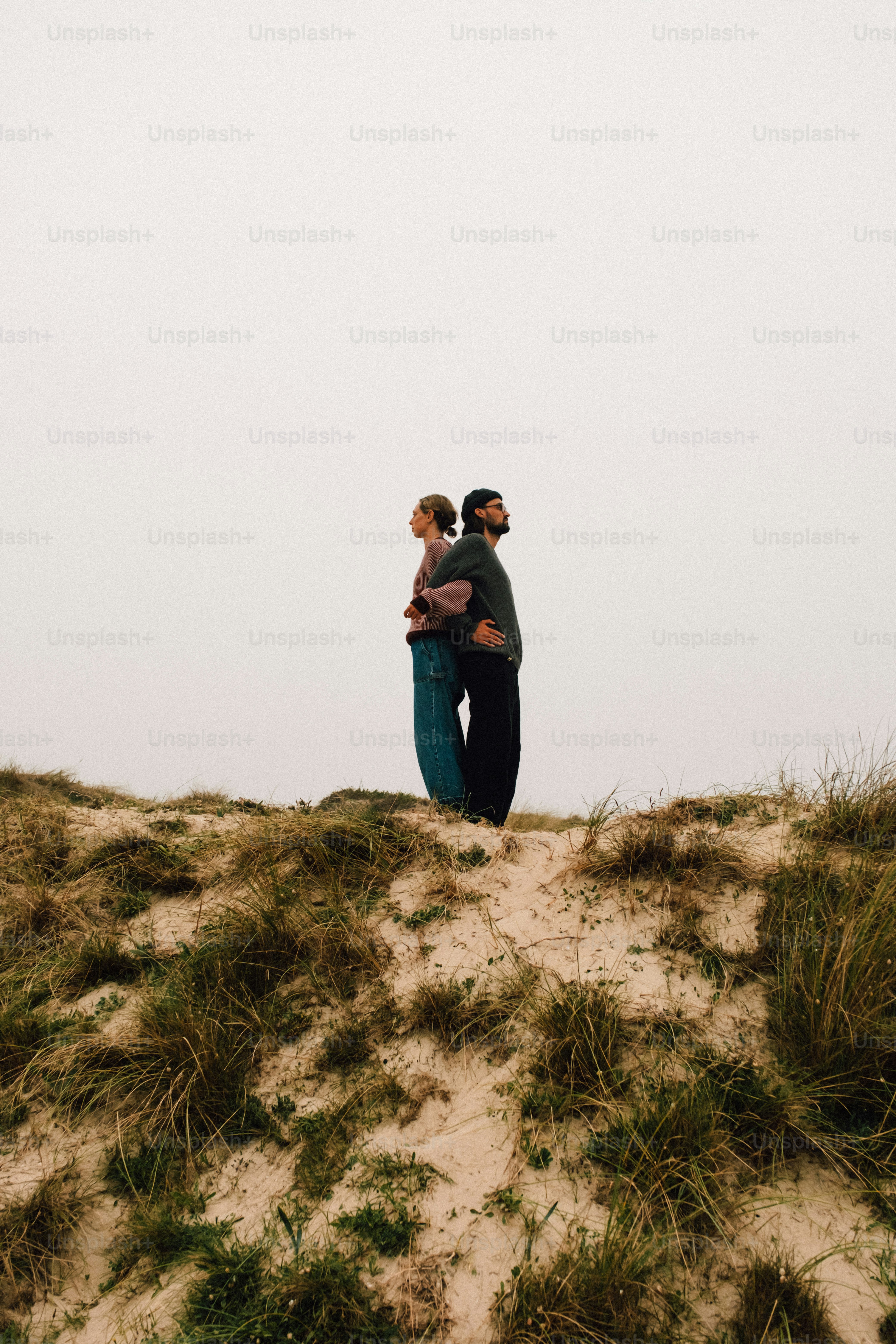 草が生い茂った砂丘に背中合わせに立っているカップル