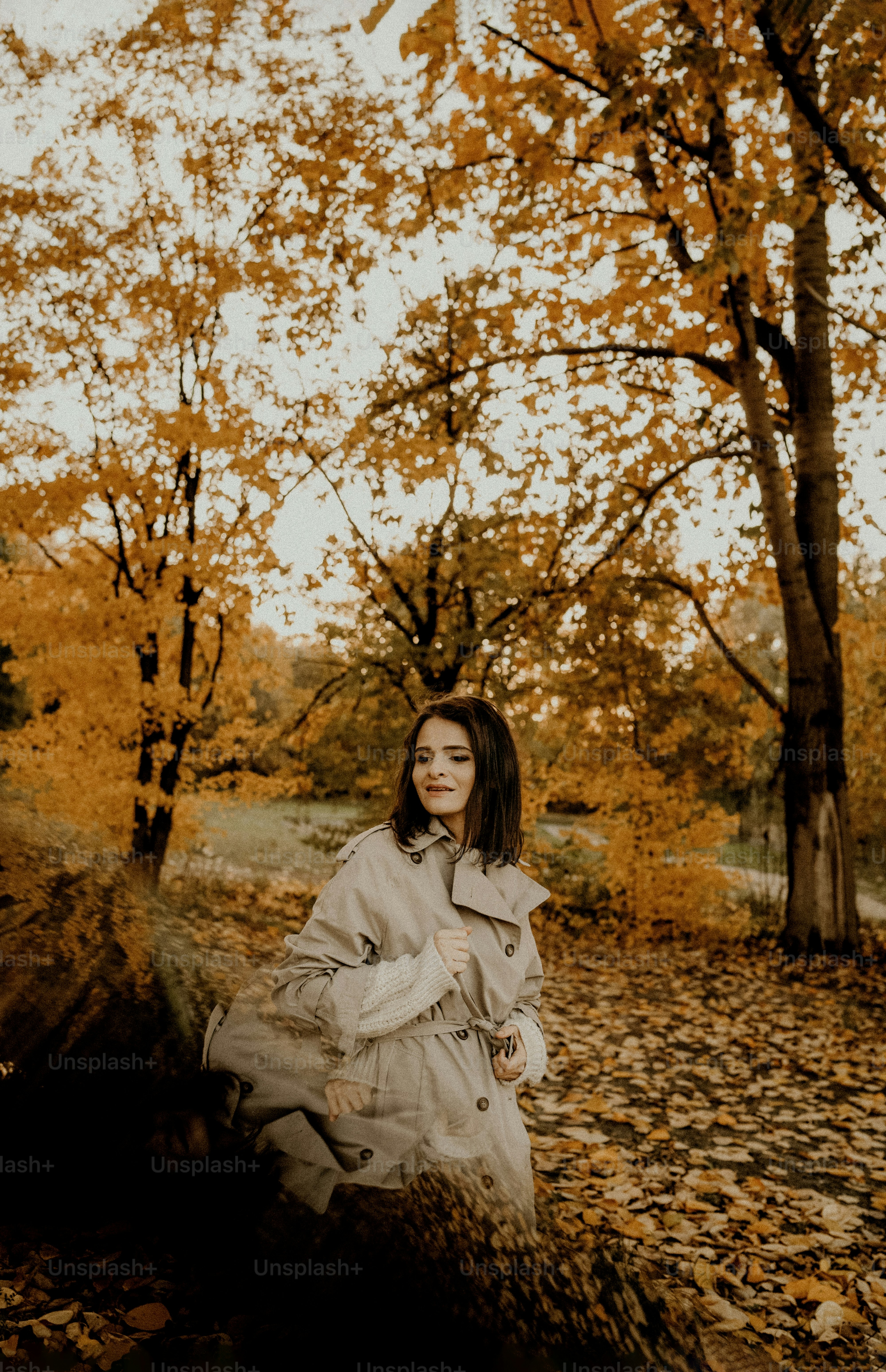 Woman in trench coat in autumn park with yellow leaves