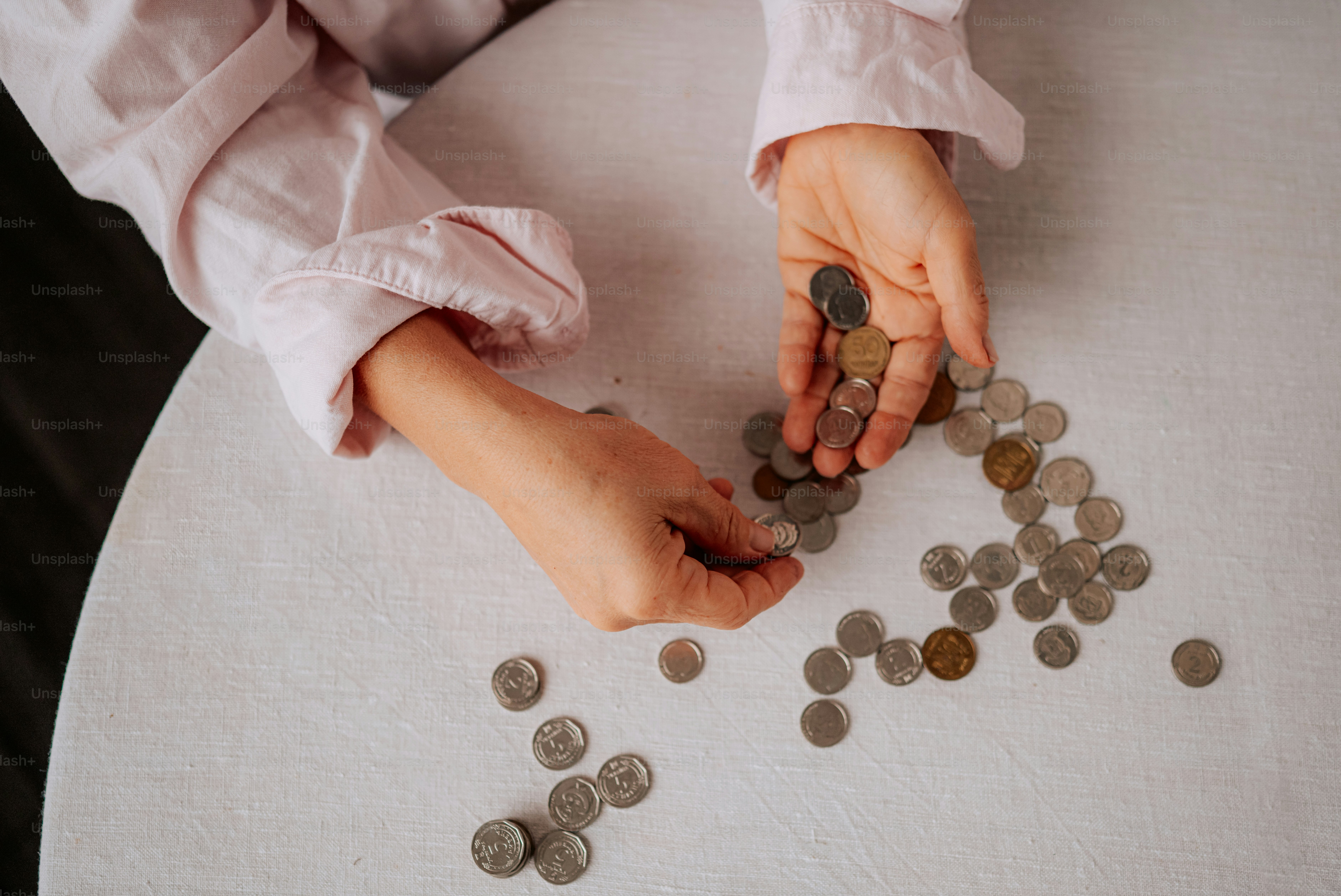 Hands sorting coins on a white table.