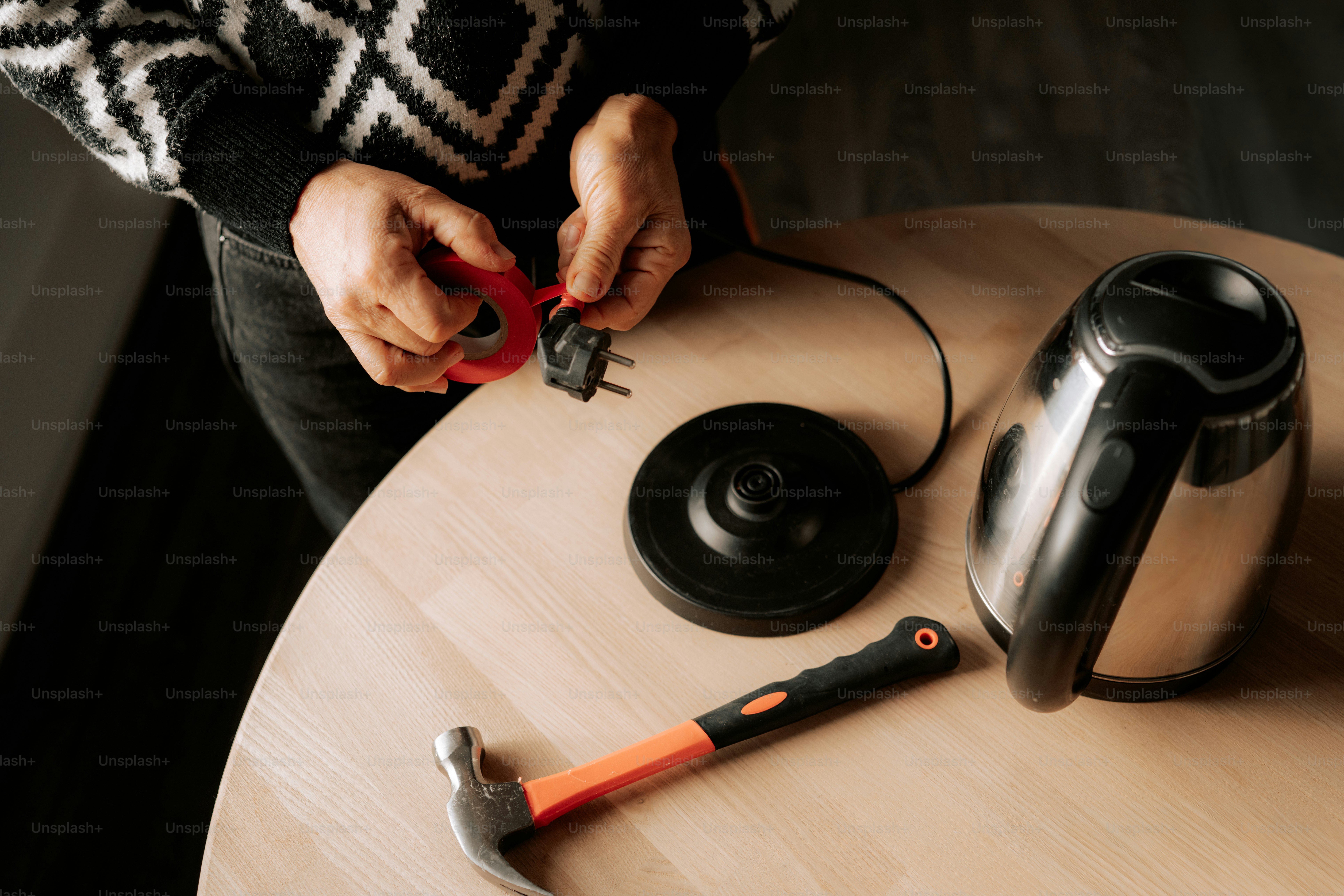 Person repairing electric kettle with tape and hammer
