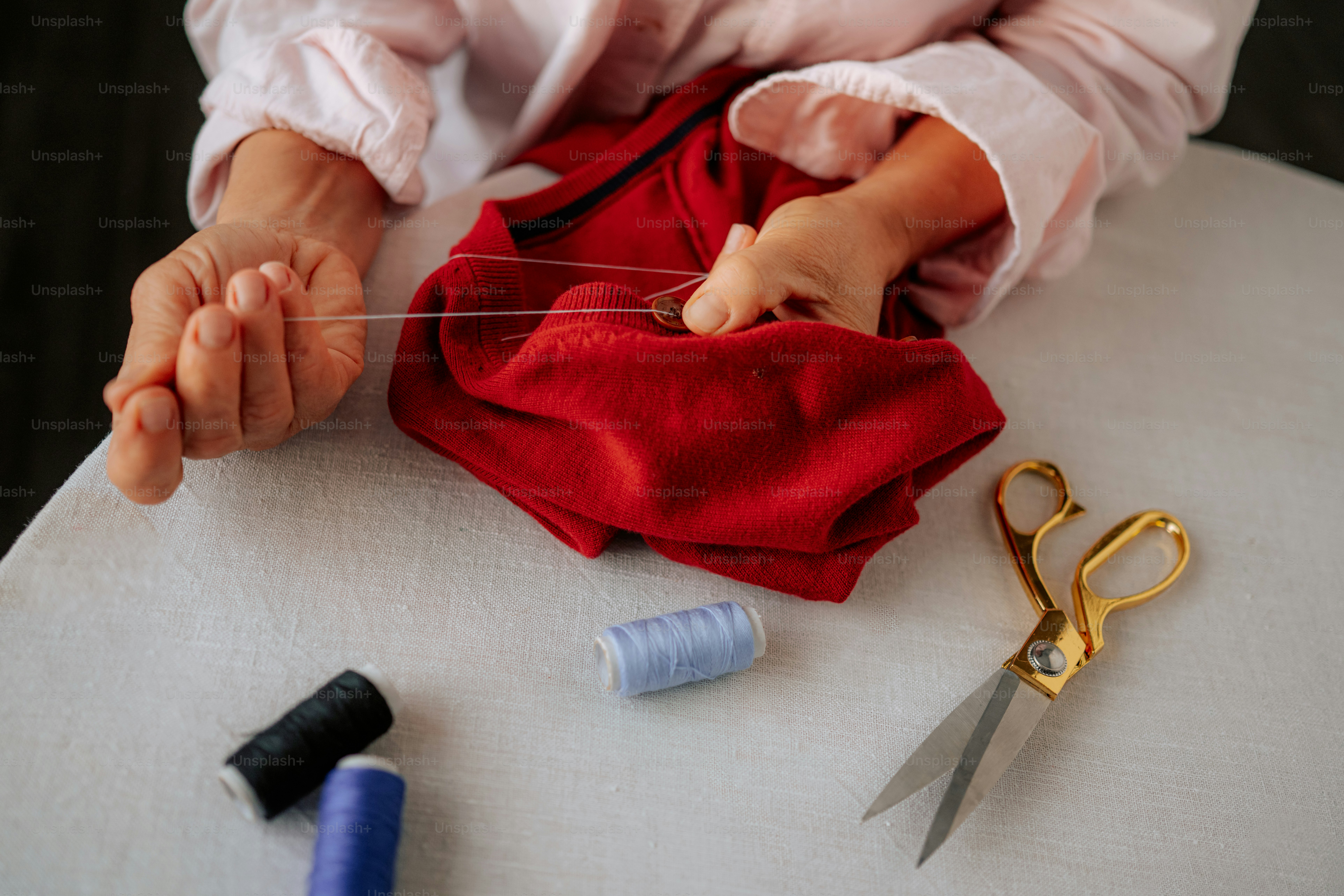 Hands sewing red fabric with thread and scissors.