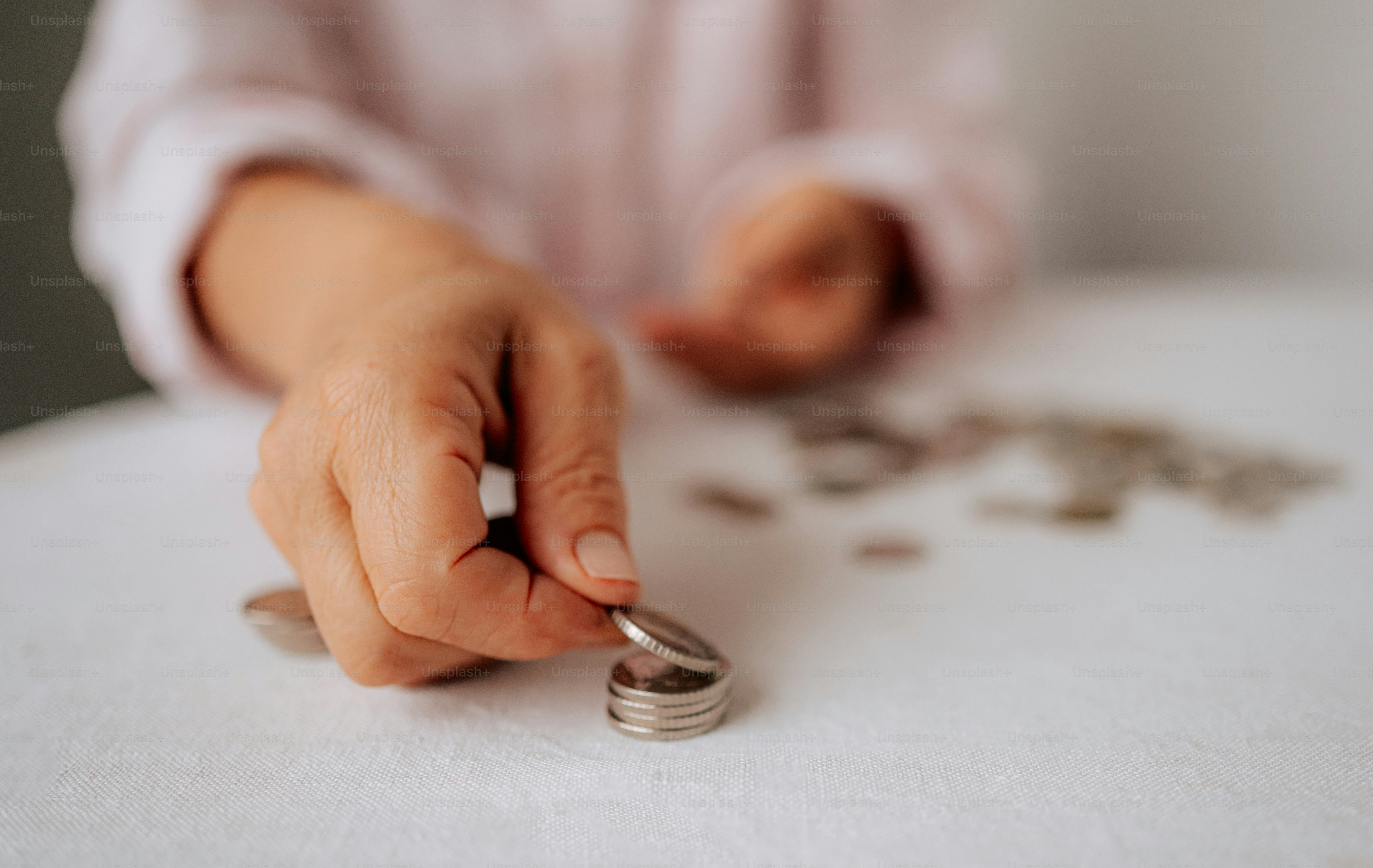 A person stacking coins on a white surface.
