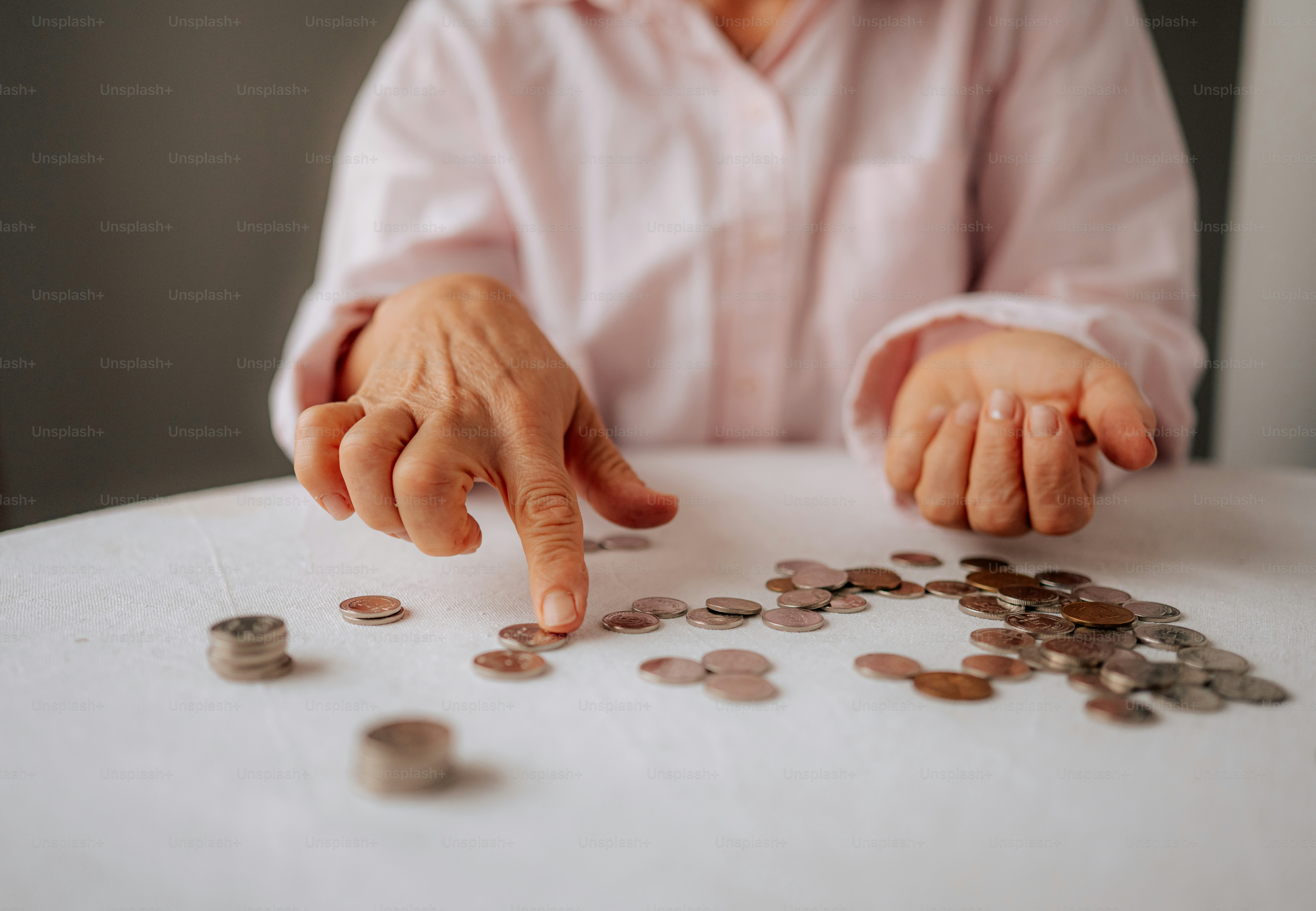 Hands counting scattered coins on a white table.