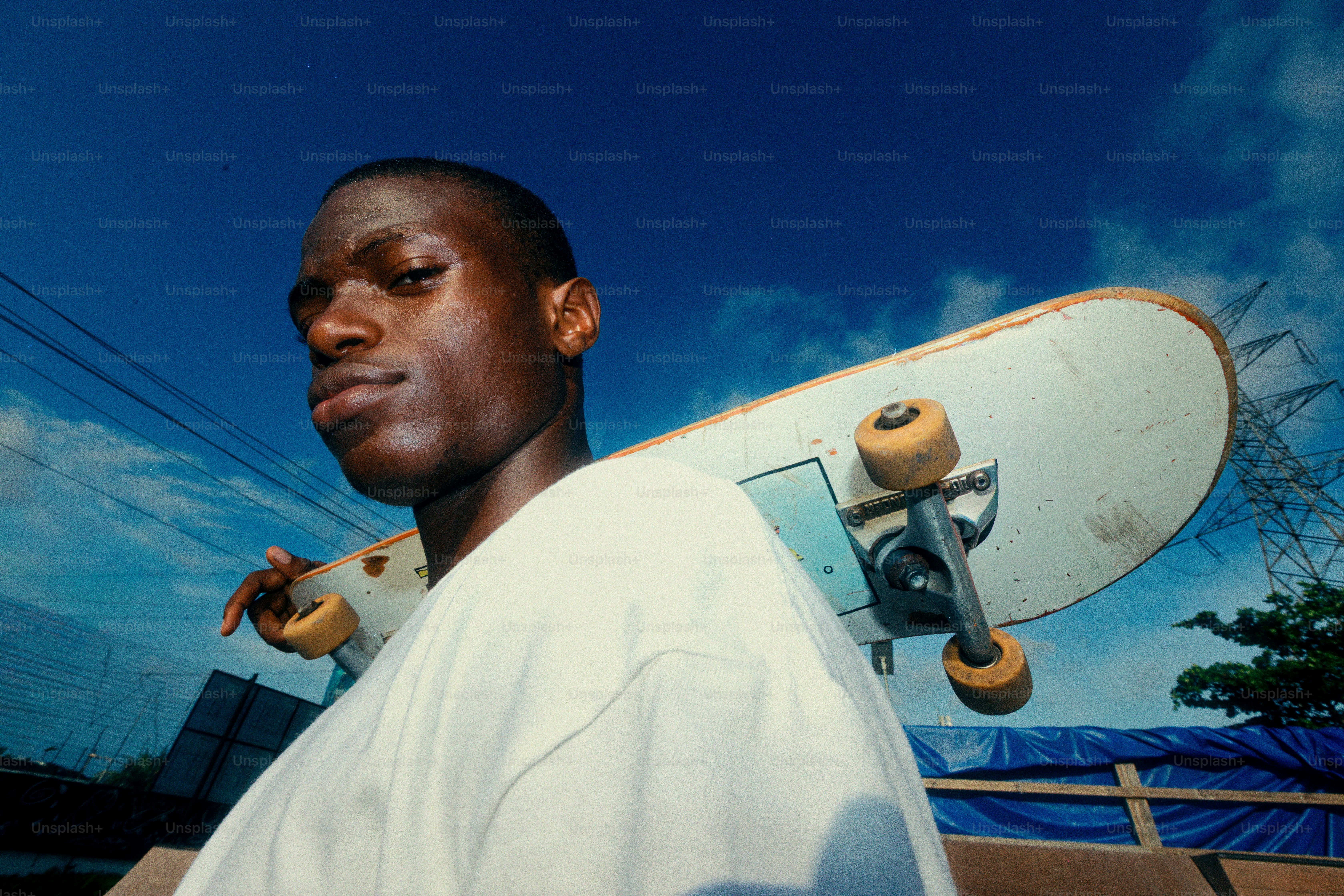 Homem novo com o skate em seu ombro sob o céu azul