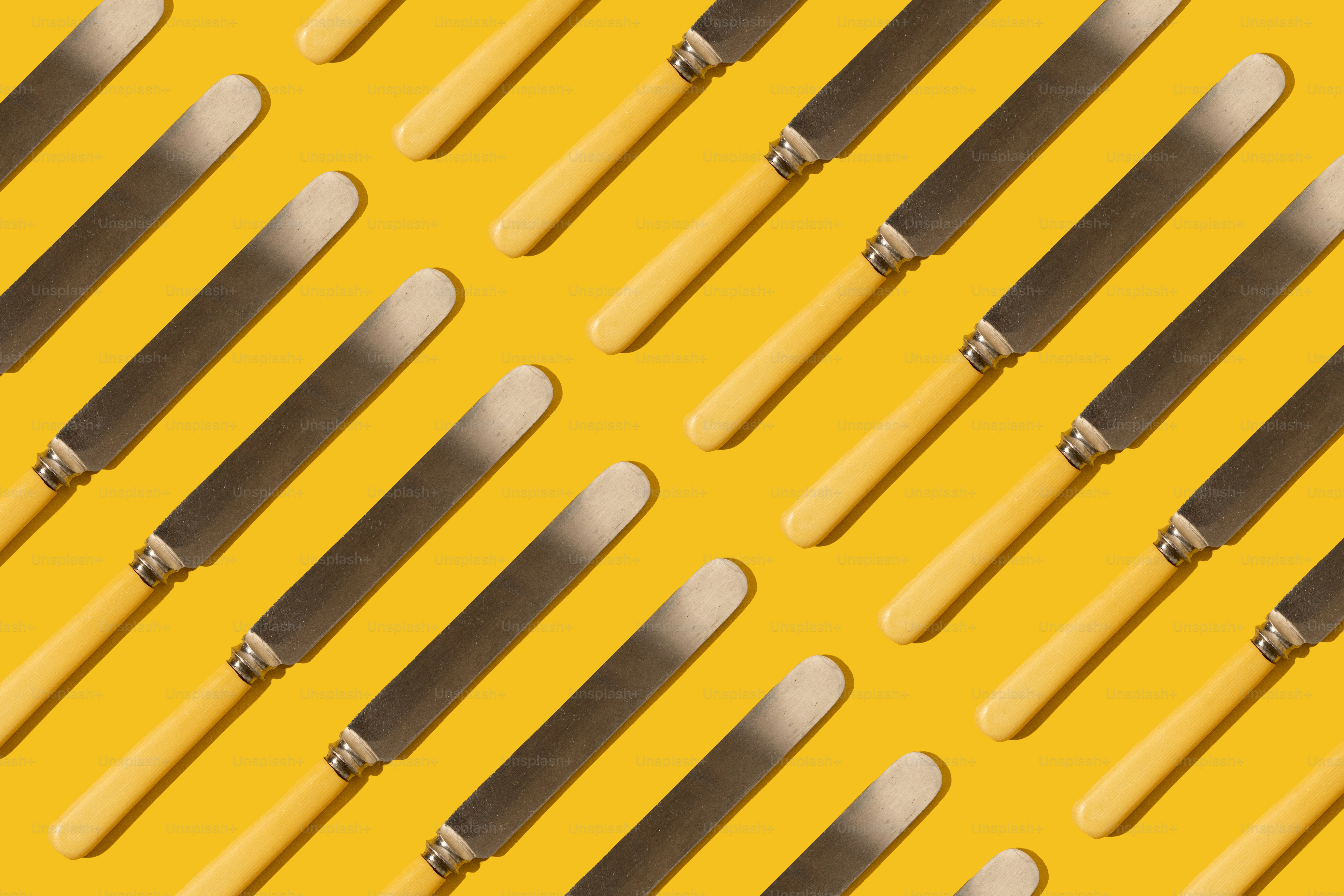 Coltelli dal manico giallo disposti in diagonale su sfondo giallo.