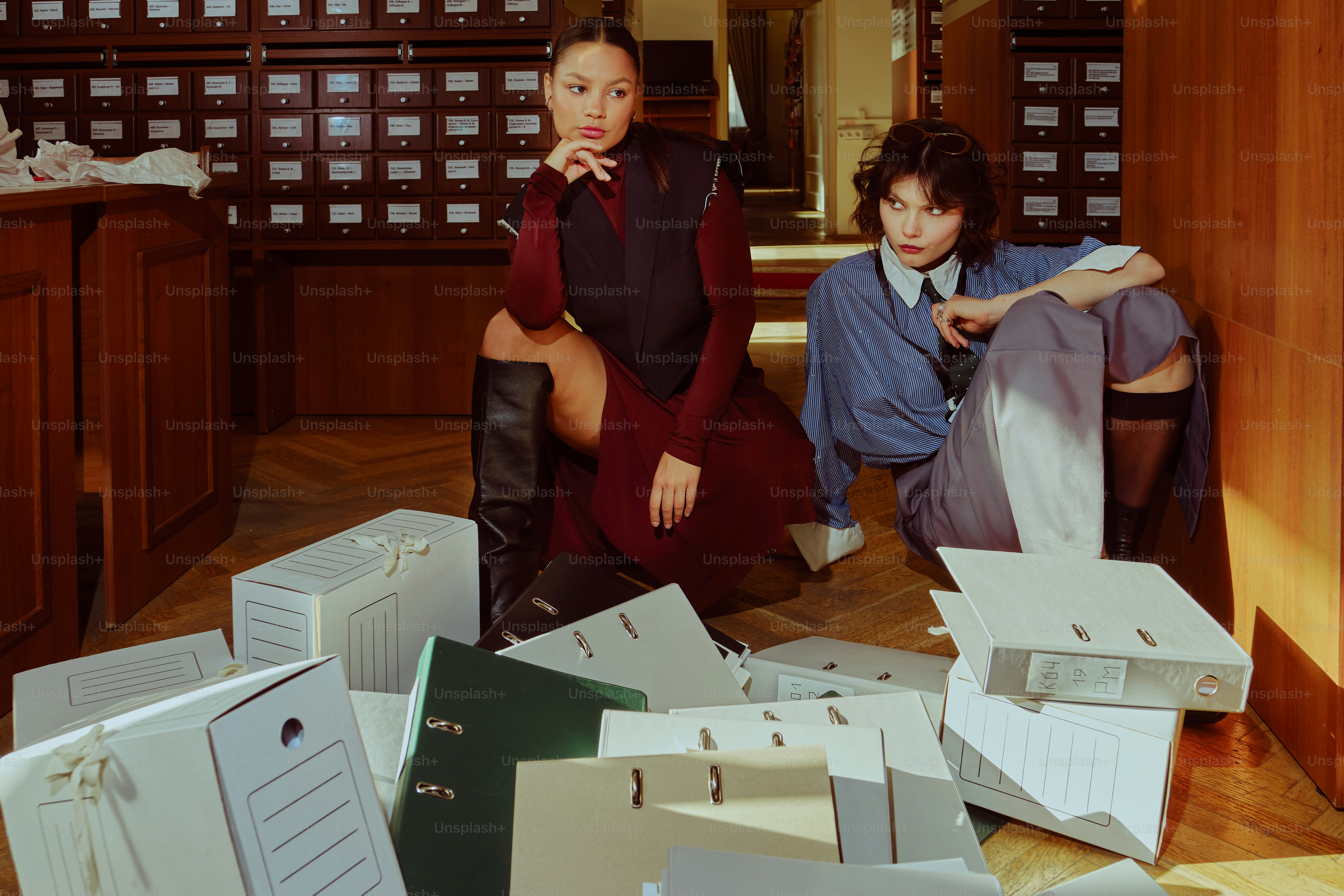 Two women sitting among scattered files in a library. photo – Office ...